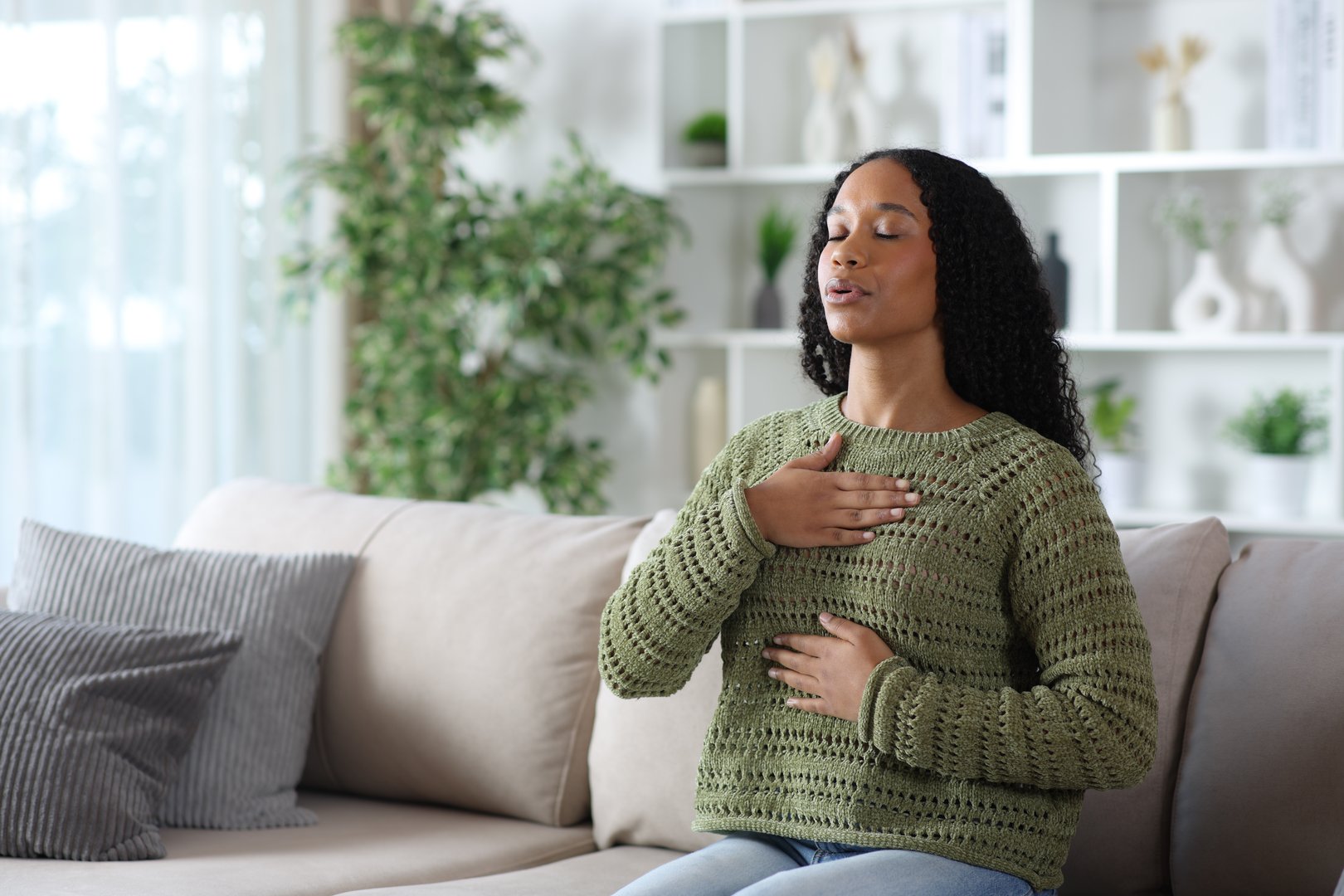 Black woman in green doing breathing exercise sitting on a couch at home