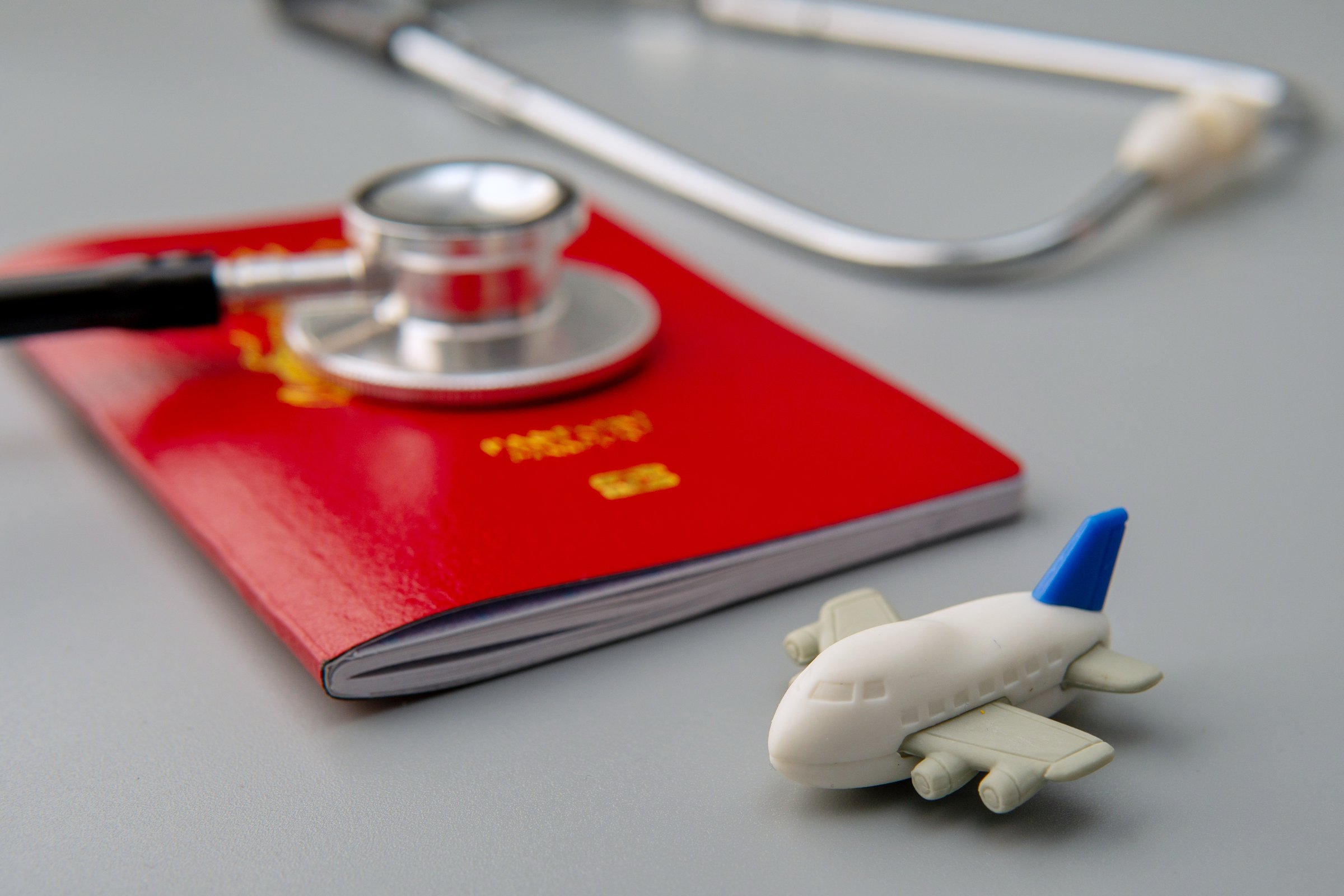 A close-up image of a passport, stethoscope, and a toy airplane. Medical tourism or the concept of traveling for healthcare concept.