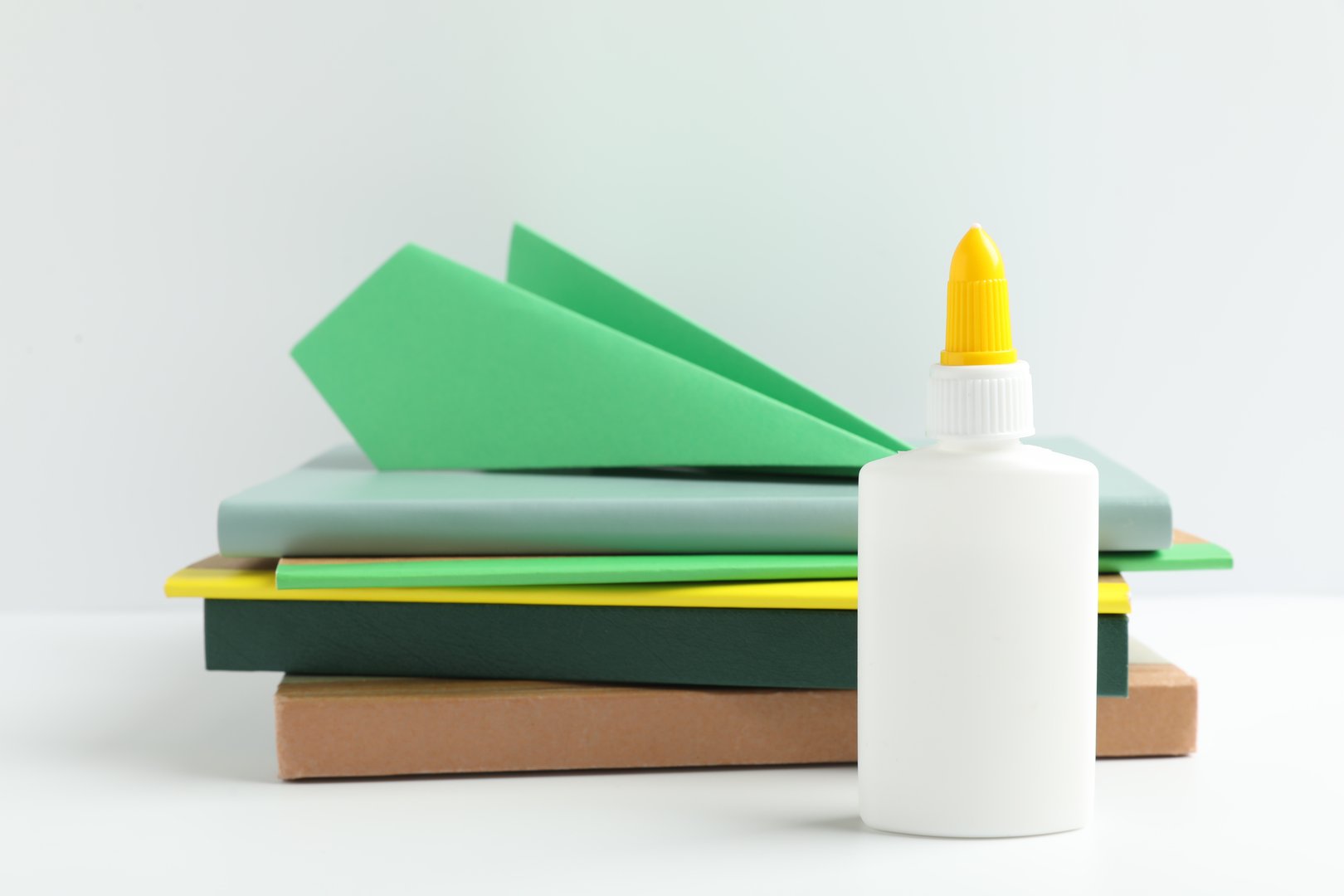 Glue, paper plane and notebooks on white table