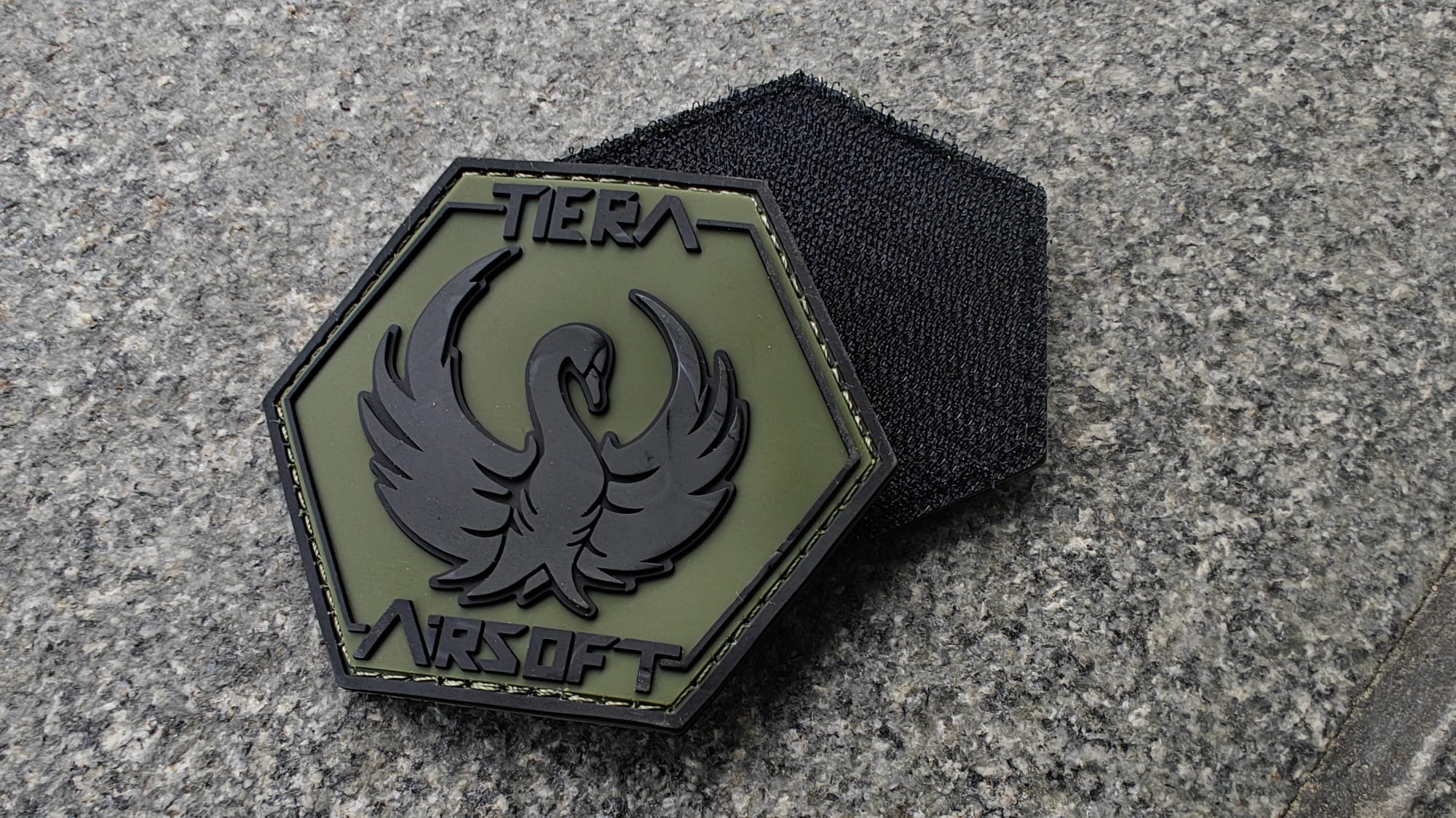 Hexagonal patch with a black phoenix design, labeled TIER AIRSOFT, on a textured stone surface.