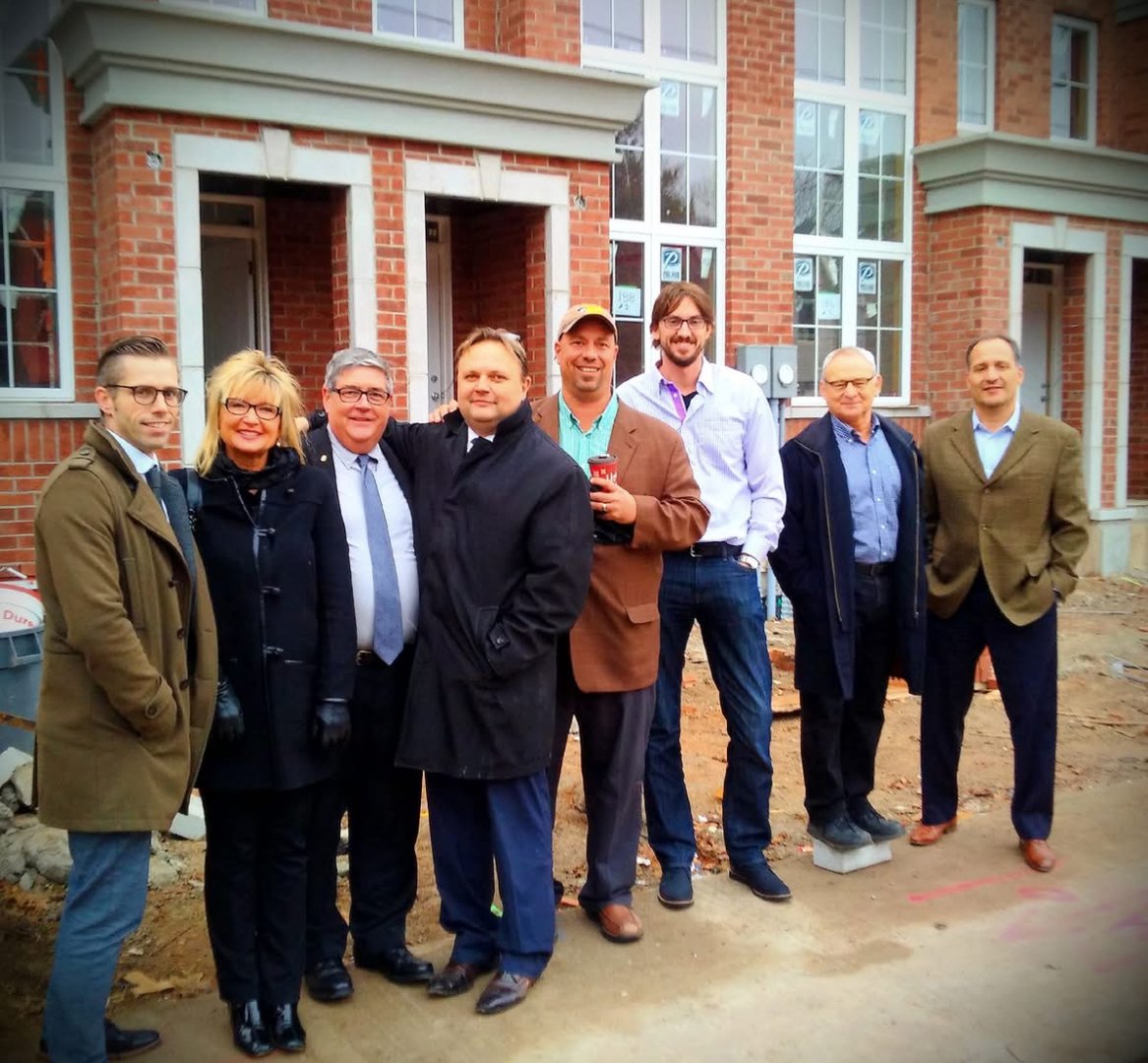 Group of people in business attire posing in front of a construction site with brick buildings in the background.
