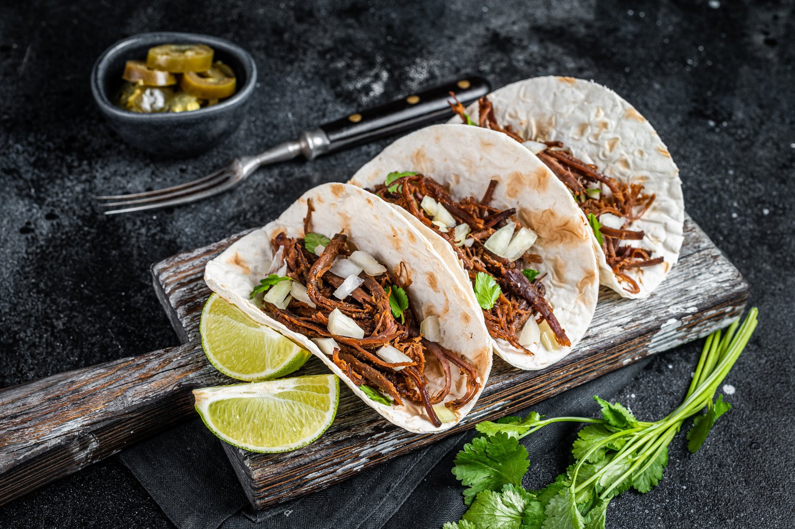 Pork carnitas tacos on corn tortillas with onion and lime. Black background. Top view.
