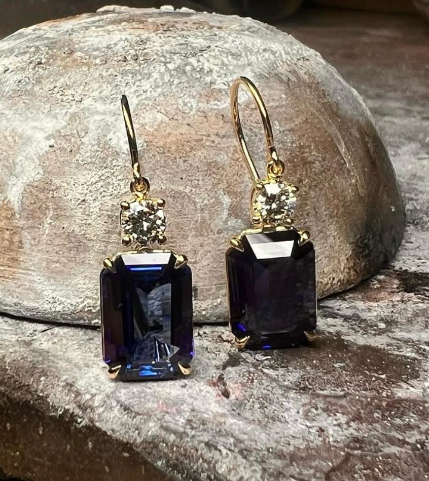 Gold drop earrings with large blue gemstones and small clear stones on a textured surface.