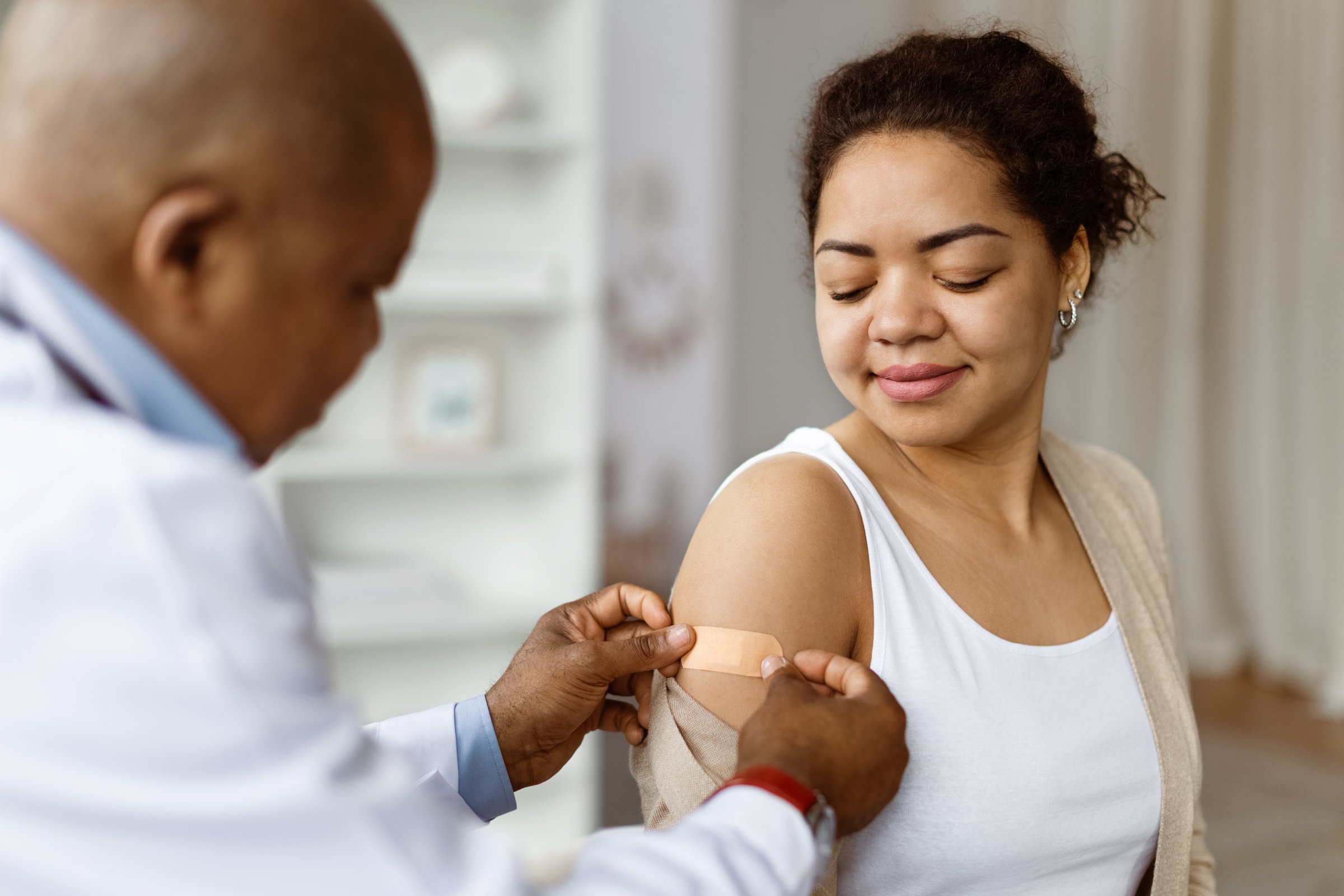 Doctor applying adhesive bandage to patients upper arm after vaccination