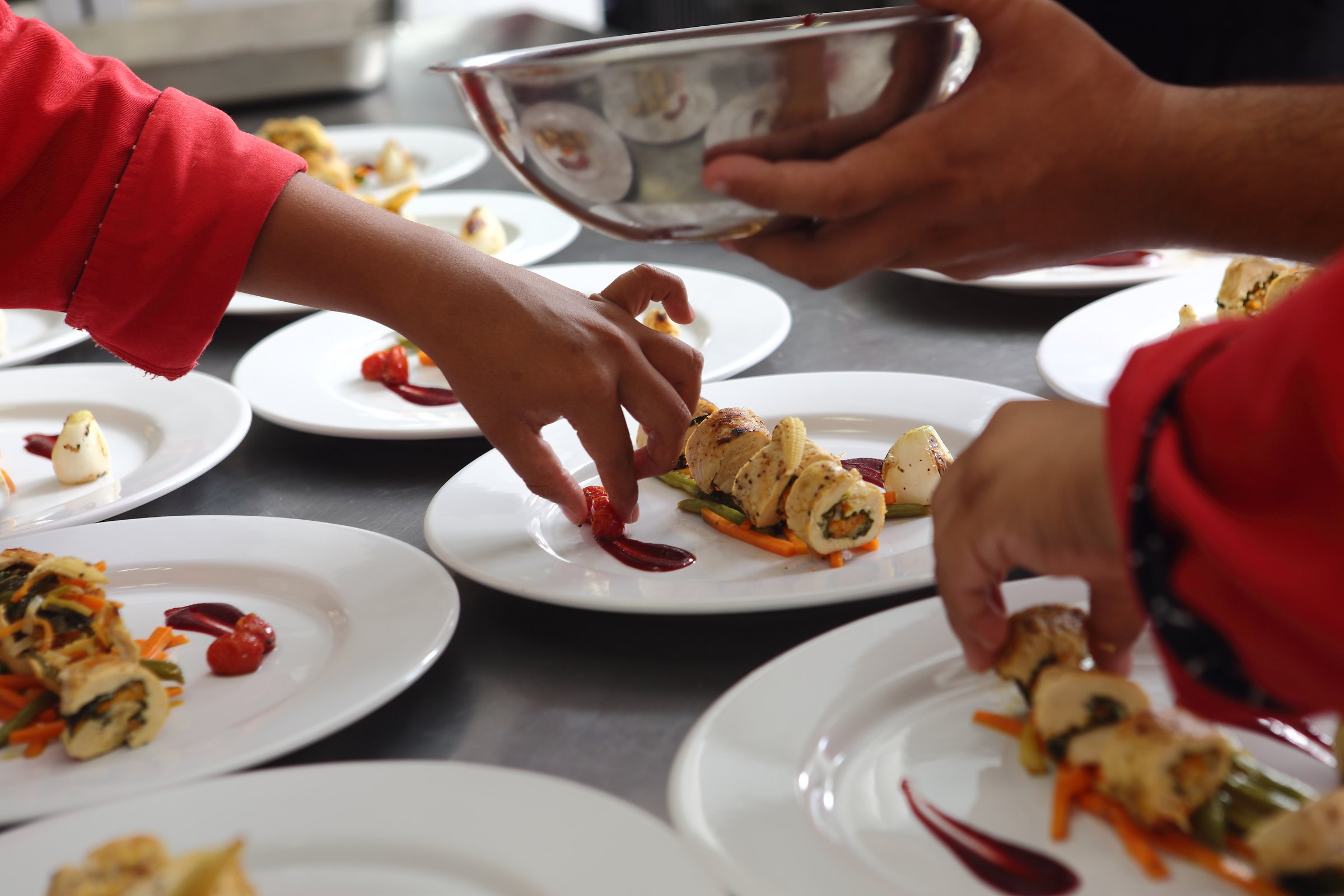 A group of several chefs prepare various dishes for a banquet that includes roasted chicken fillet and dessert.