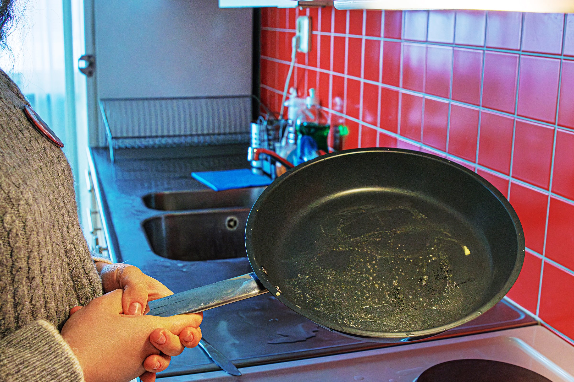 A cropped view of woman holding a teflon frying pan with oil over an electric stove in a modern domestic kitchen