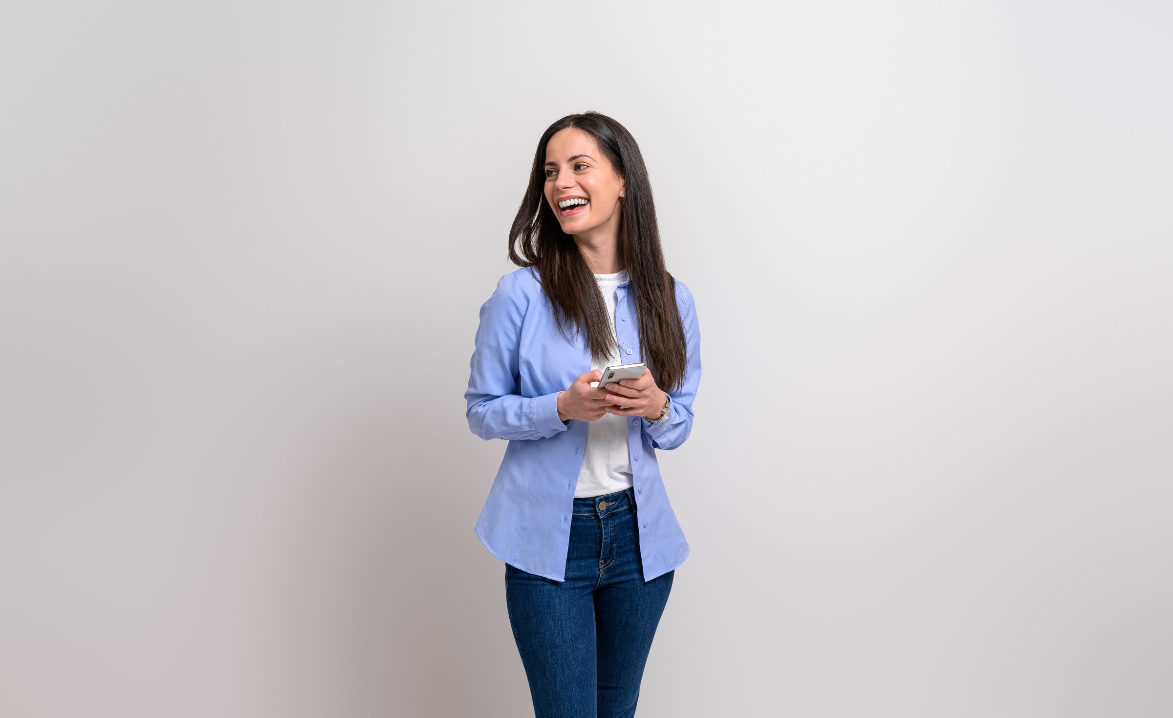 Laughing businesswoman texting over smart phone and looking away on isolated white background