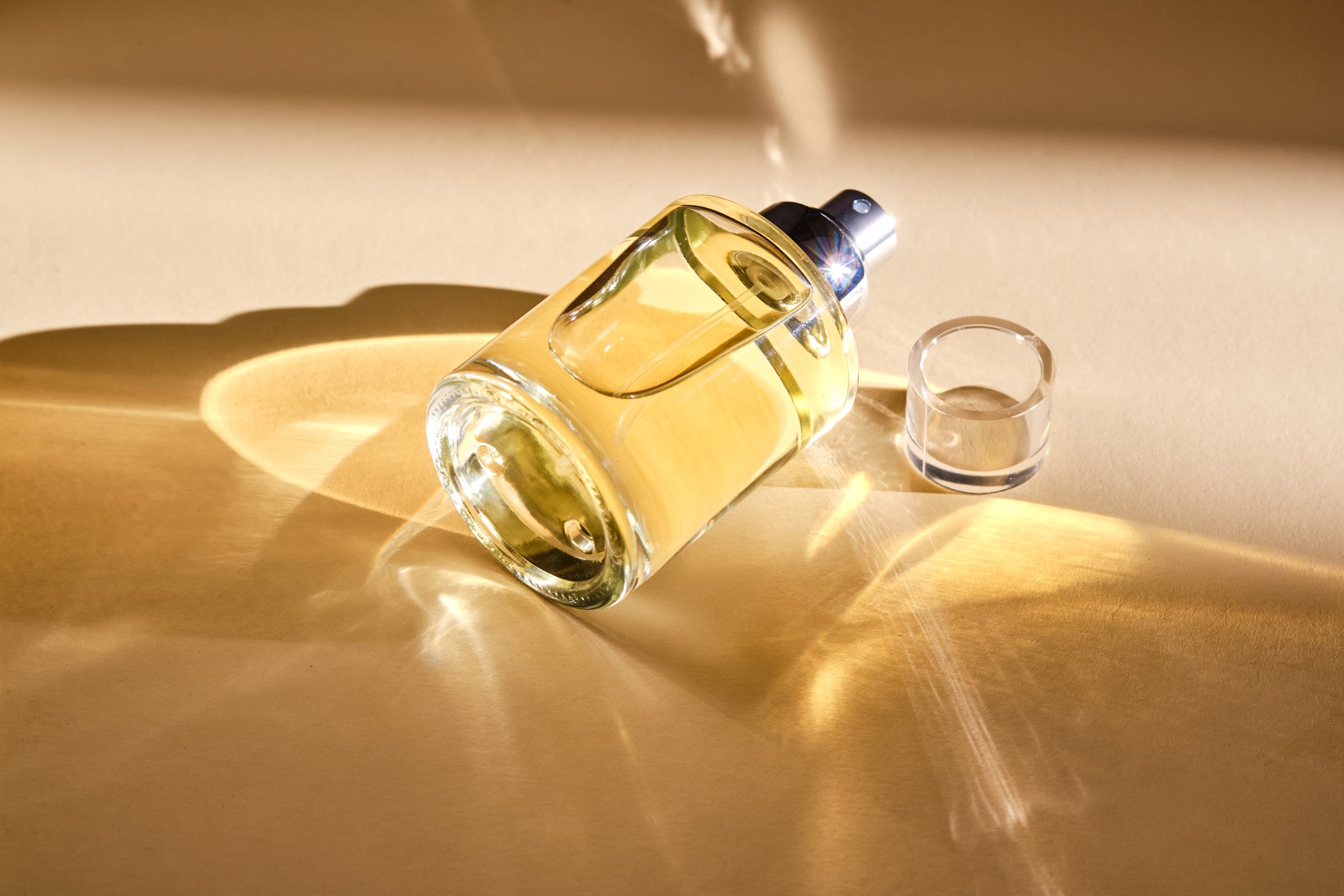 Perfume on a beige background in the rays of bright sun with beautiful highlights. High quality photo.