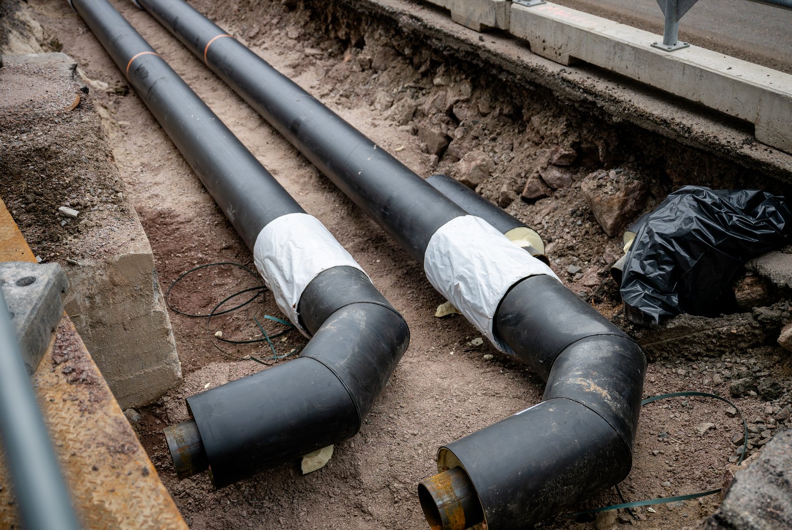 Large insulated steel pipes installed in a trench at an underground pipeline construction site.