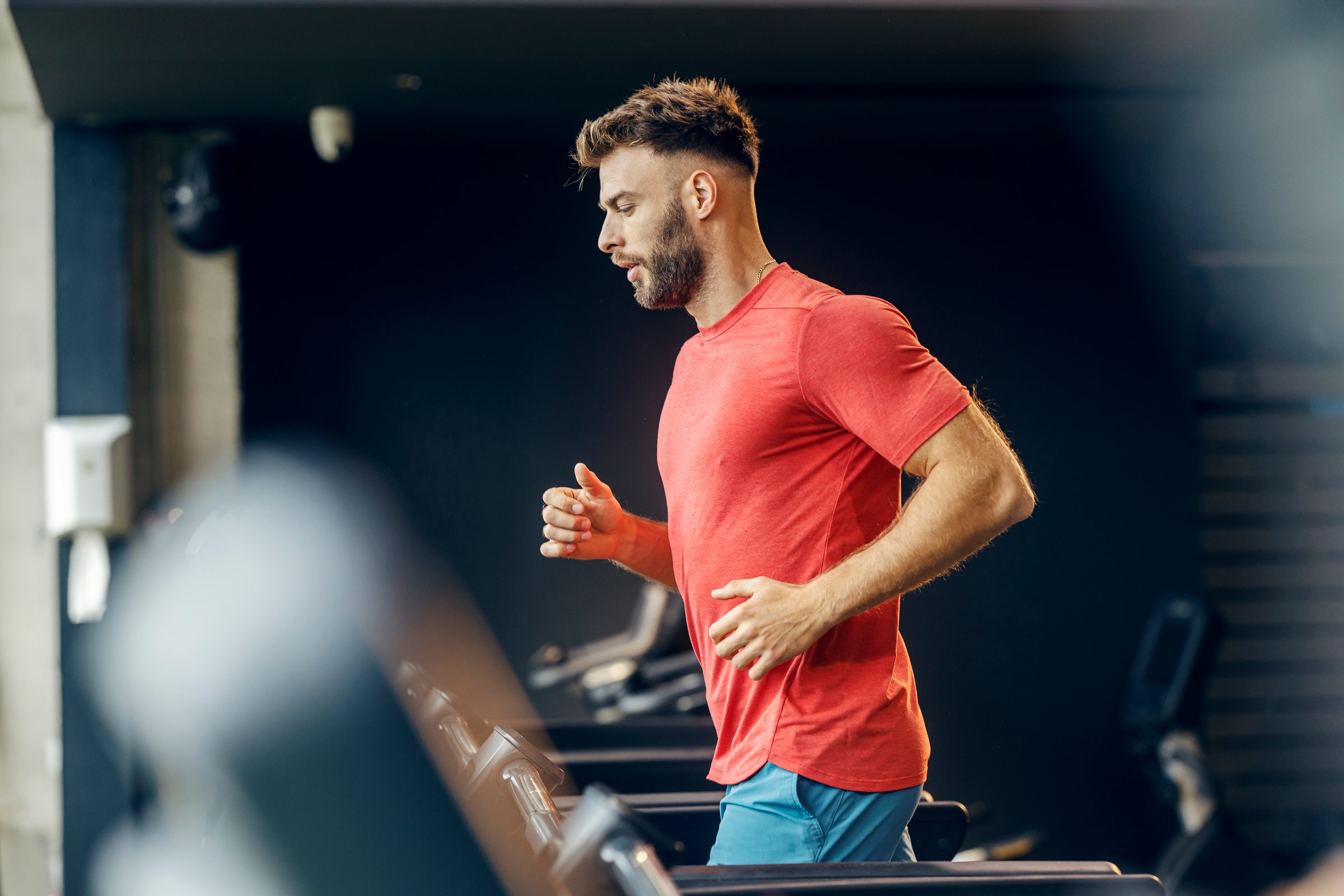 Profile view of active sportsman in excellent shape practicing on treadmill at gym.