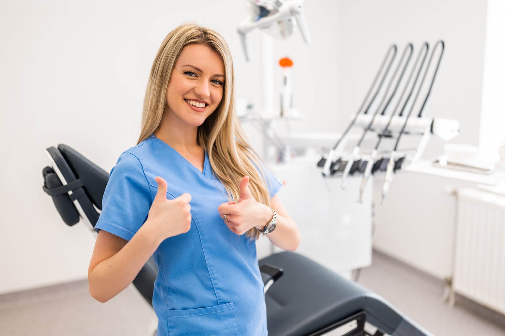 Portrait of happy dentist in dentist's office. Confident adult woman working in a dental clinic. She is showing thumbs up.