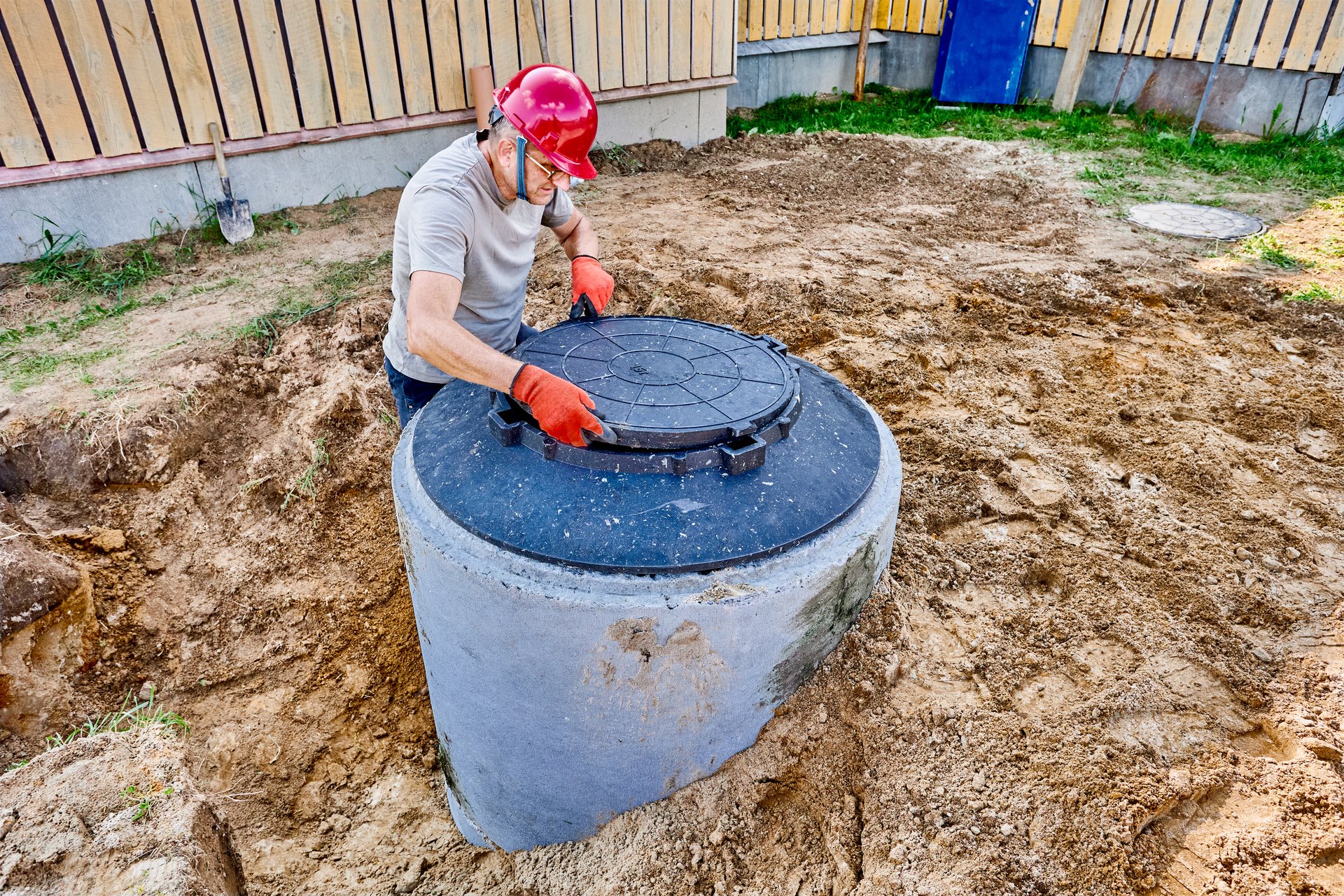 Plumber installs support ring and manhole cover on concrete septic tank in sewerage system of private country house.