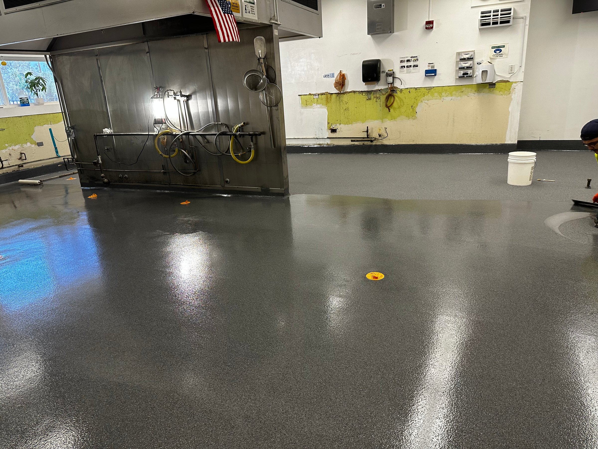 Freshly installed, shiny industrial flooring in a workshop with tools, equipment, and an American flag on the wall.