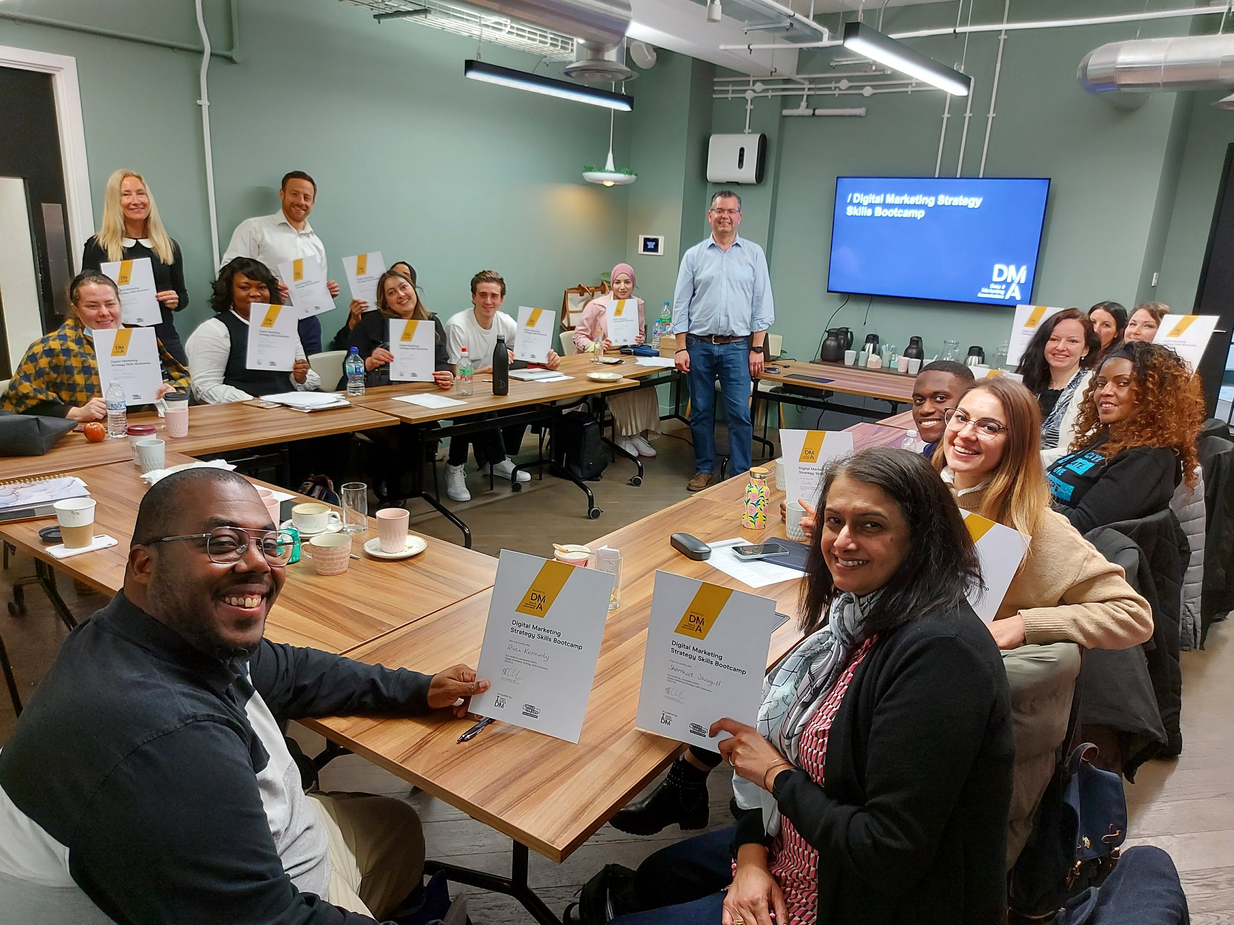 Group of people in a meeting room holding certificates, with a presentation screen displaying Digital Marketing Strategy.