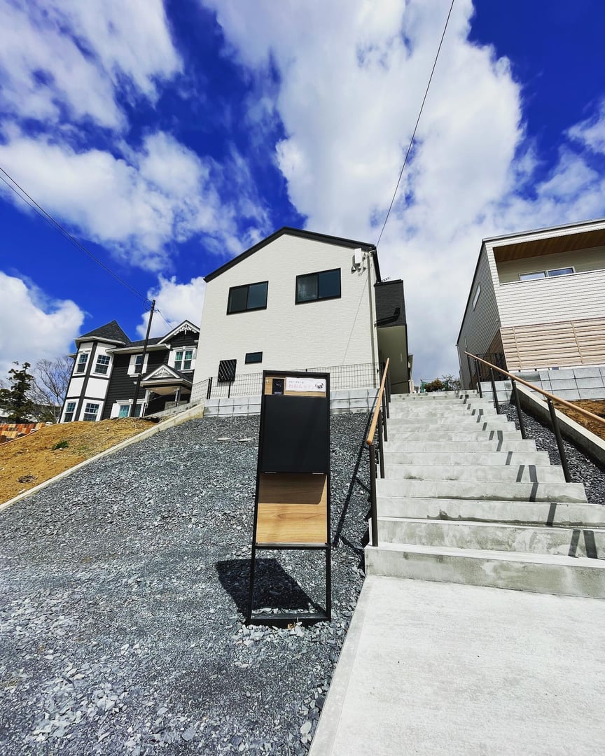 Modern white house on a hillside with a staircase and a signpost in the foreground under a blue sky with clouds.