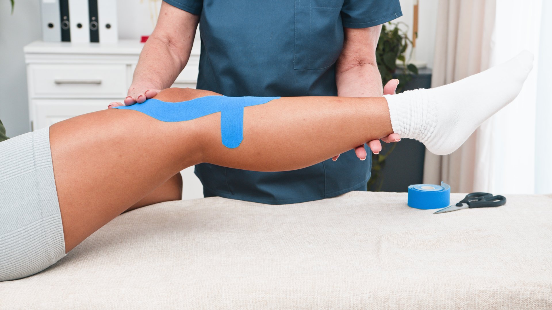 A dedicated senior physiotherapist meticulously applies supportive kinesiology tape to the knee of a young Black client.