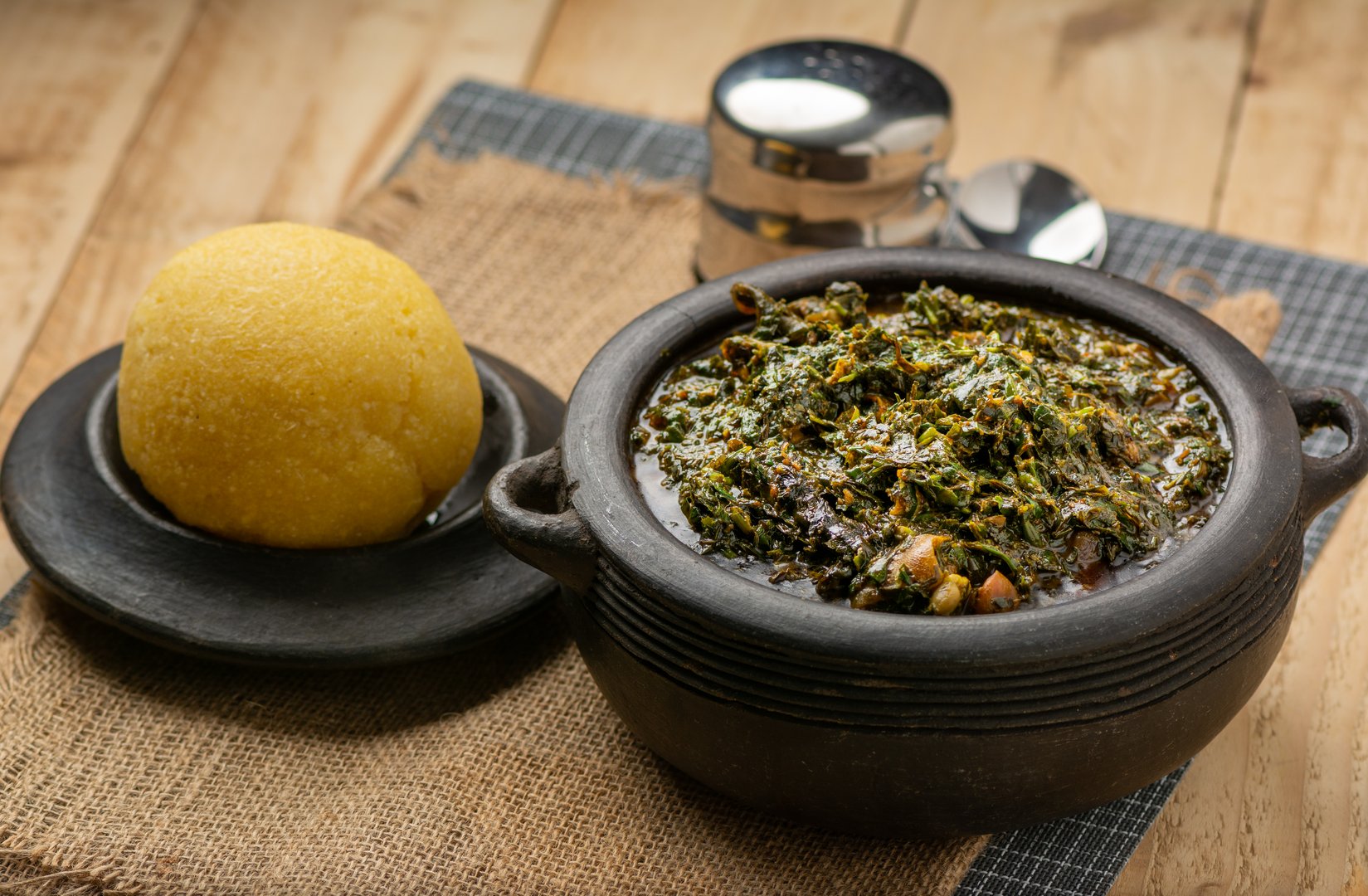 Efik Afang soup Nigerian served in a clay bowl with garri on awooden background