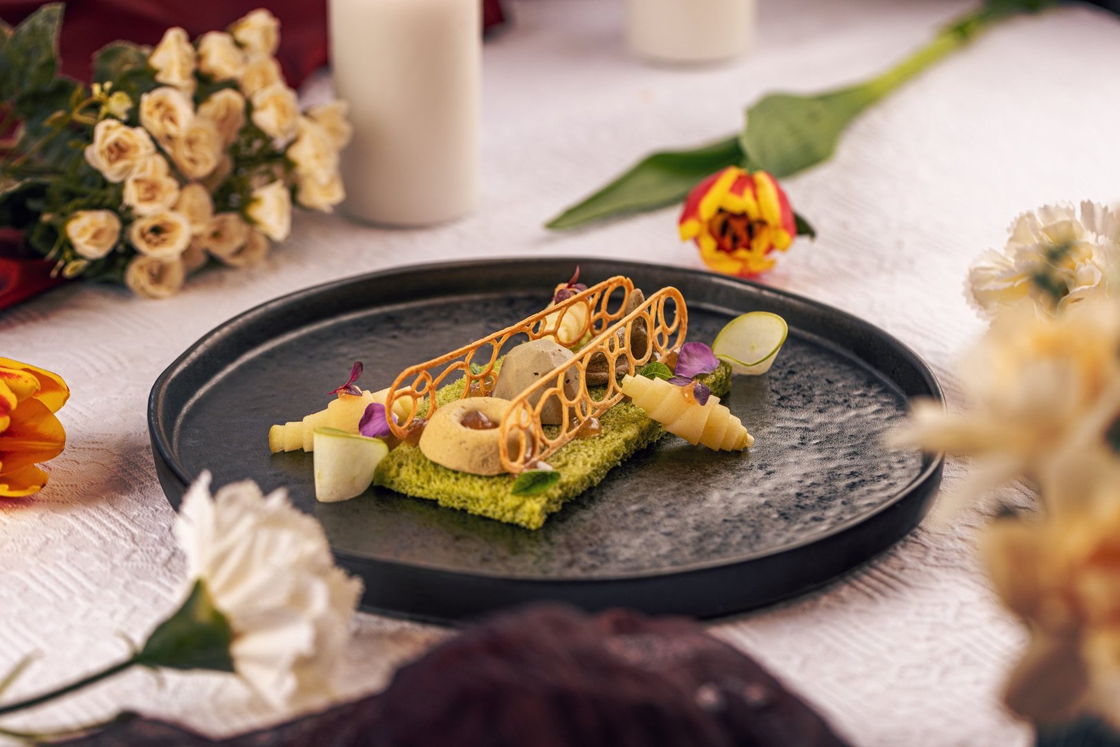 Gourmet fine dining starter plated on a stylish dark plate, garnished with edible flowers