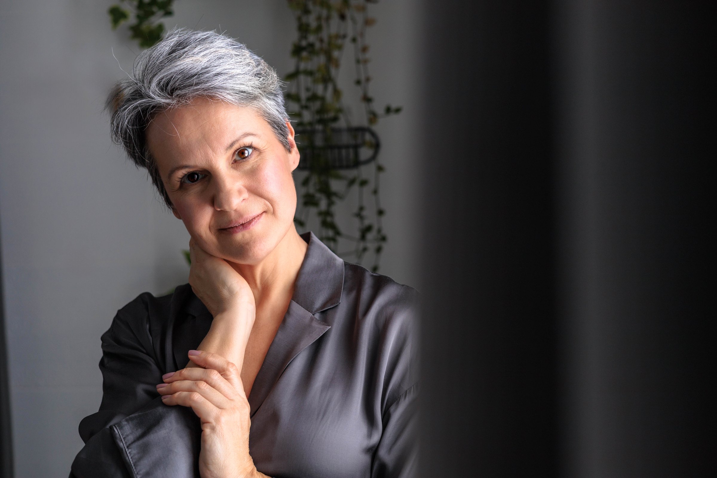 Mature beautiful woman during menopause with gray hair posing. Portrait of pensioner in silk pajamas. Anti-age concept.