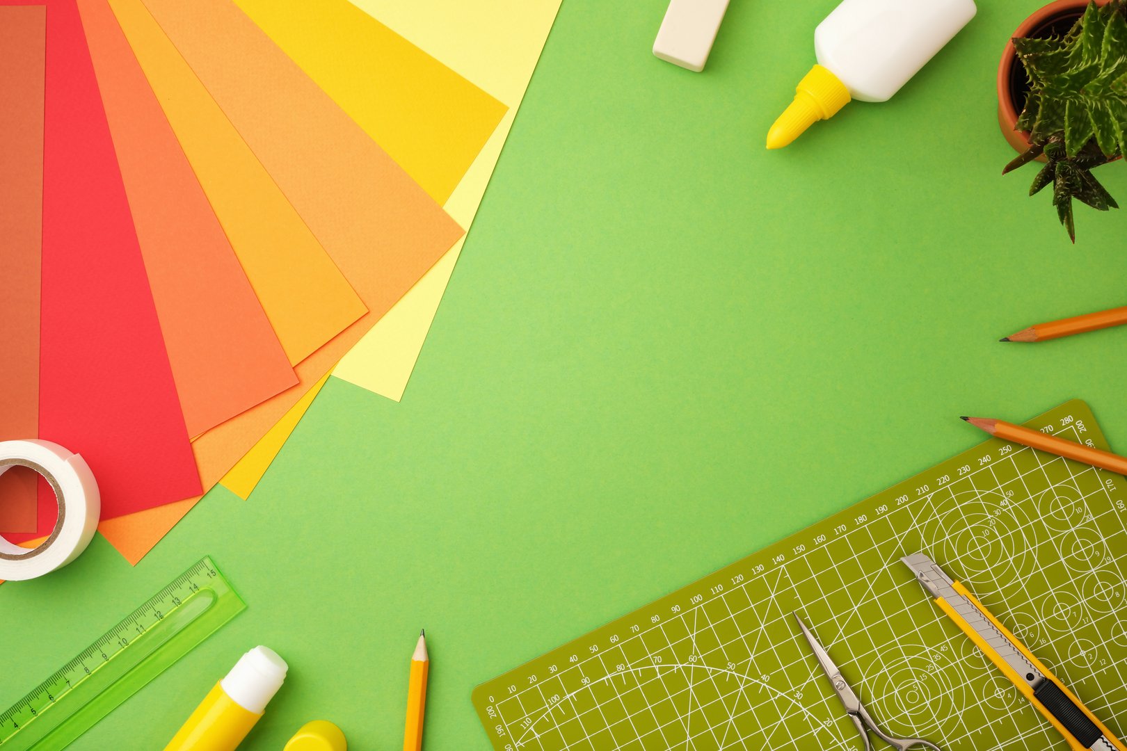 Supplies for paper art hobby: scissors, craft knife, pencil, eraser, colored paper on green background. Space for your text.
