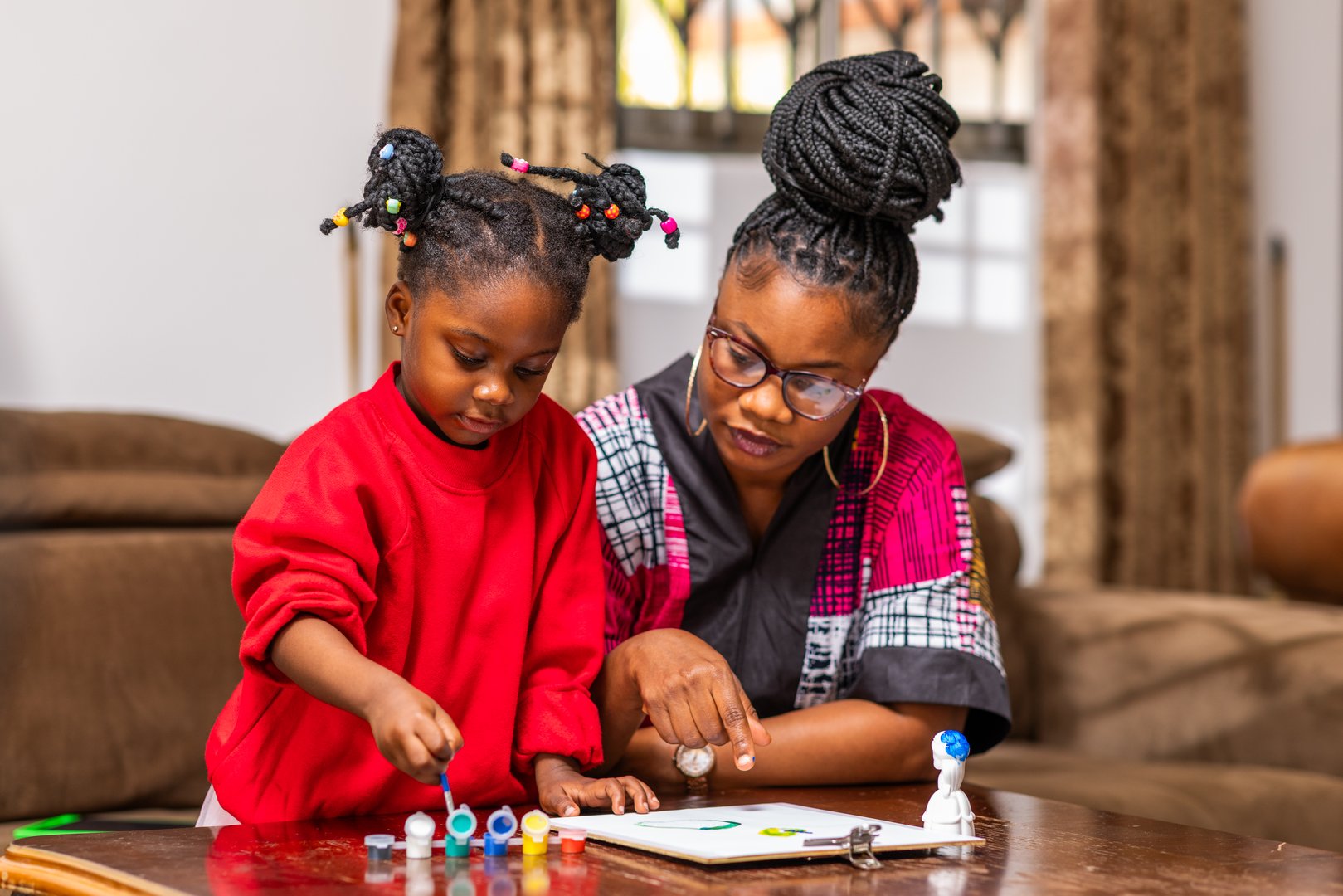 African mom spending time with her daughter doing creative art painting activity at home.