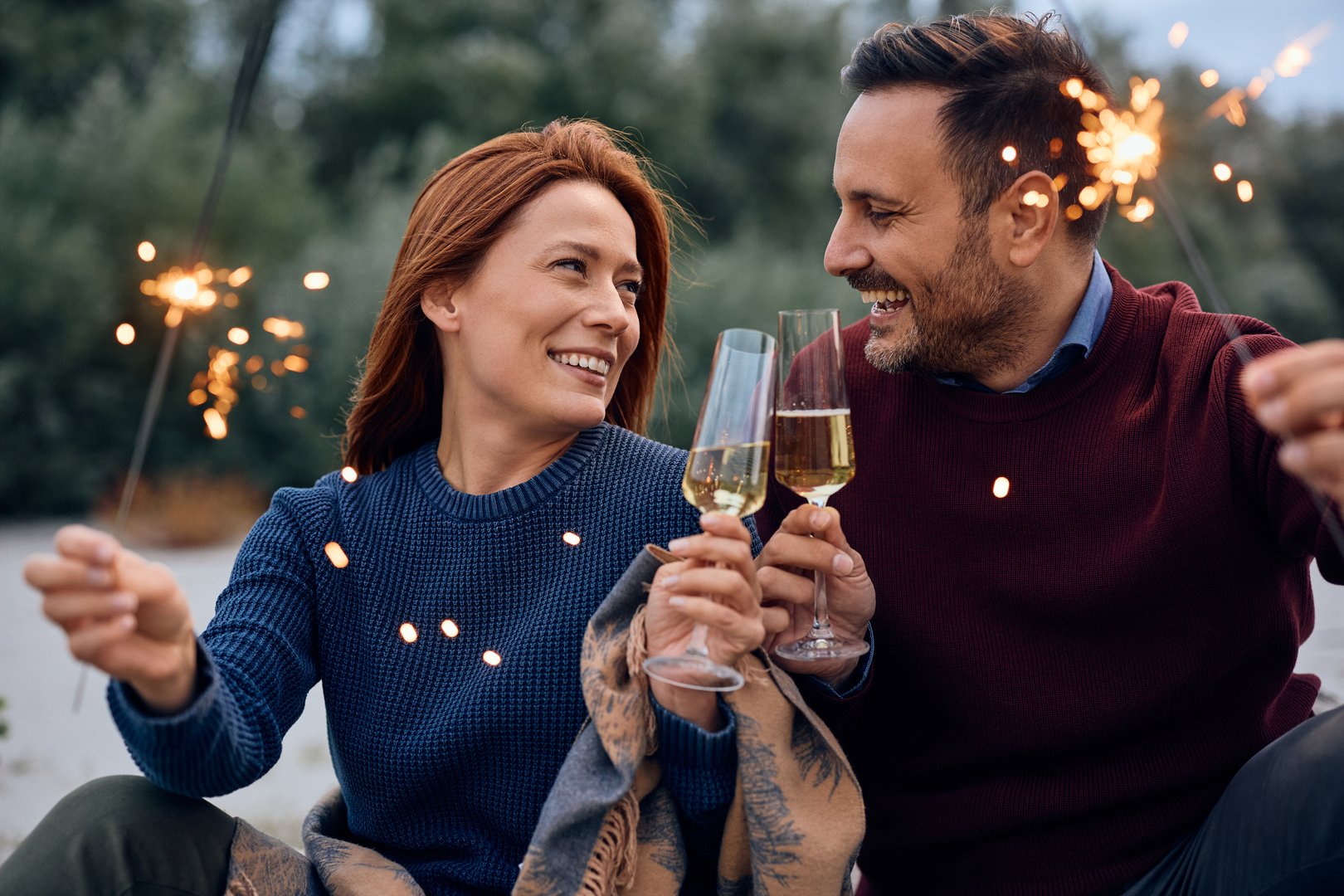 Happy couple using sparklers while toasting with champagne during autumn day outdoors.