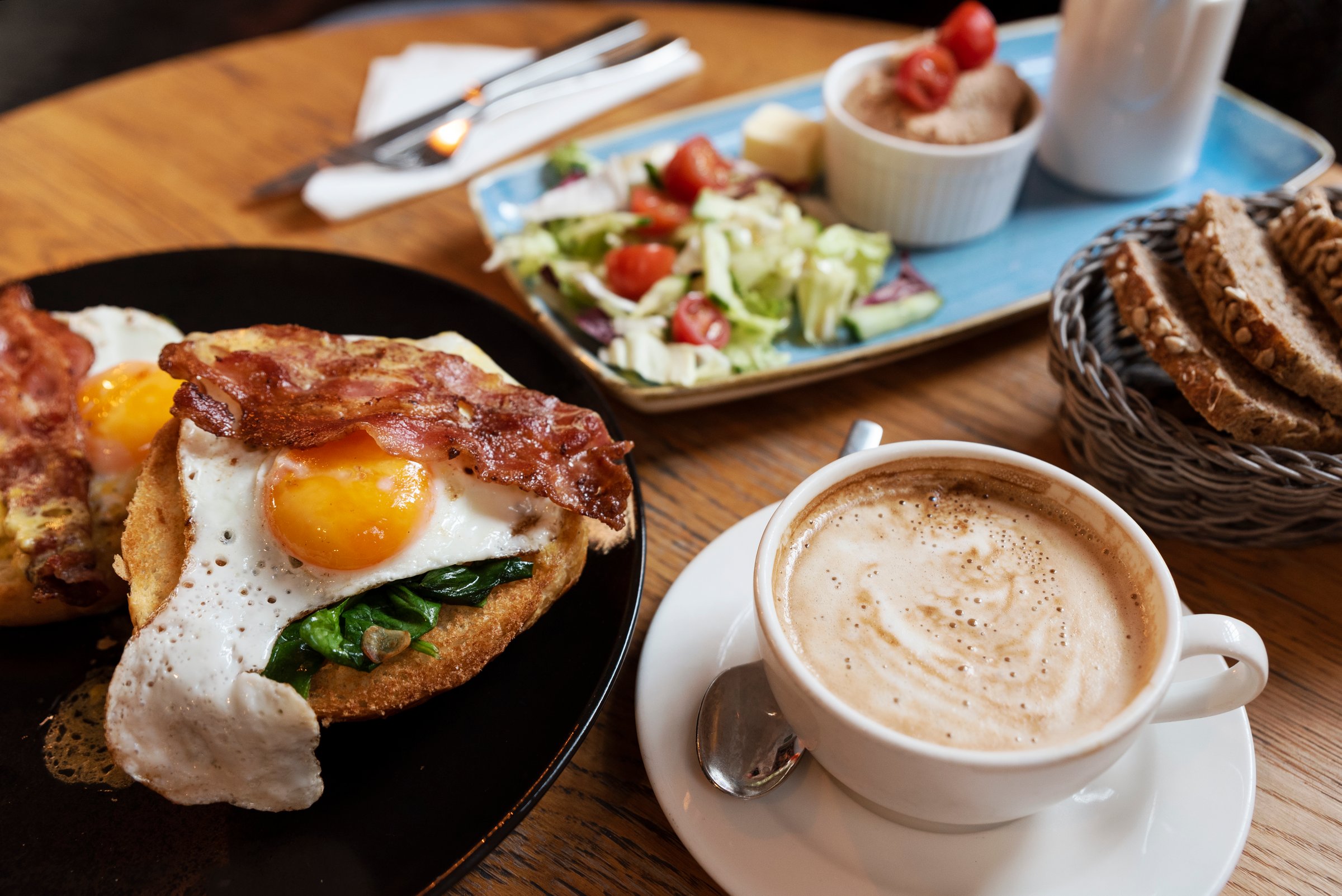 Fried egg with bacon on a plate, salad and coffee cup. English lunch in restaurant. Close-up
