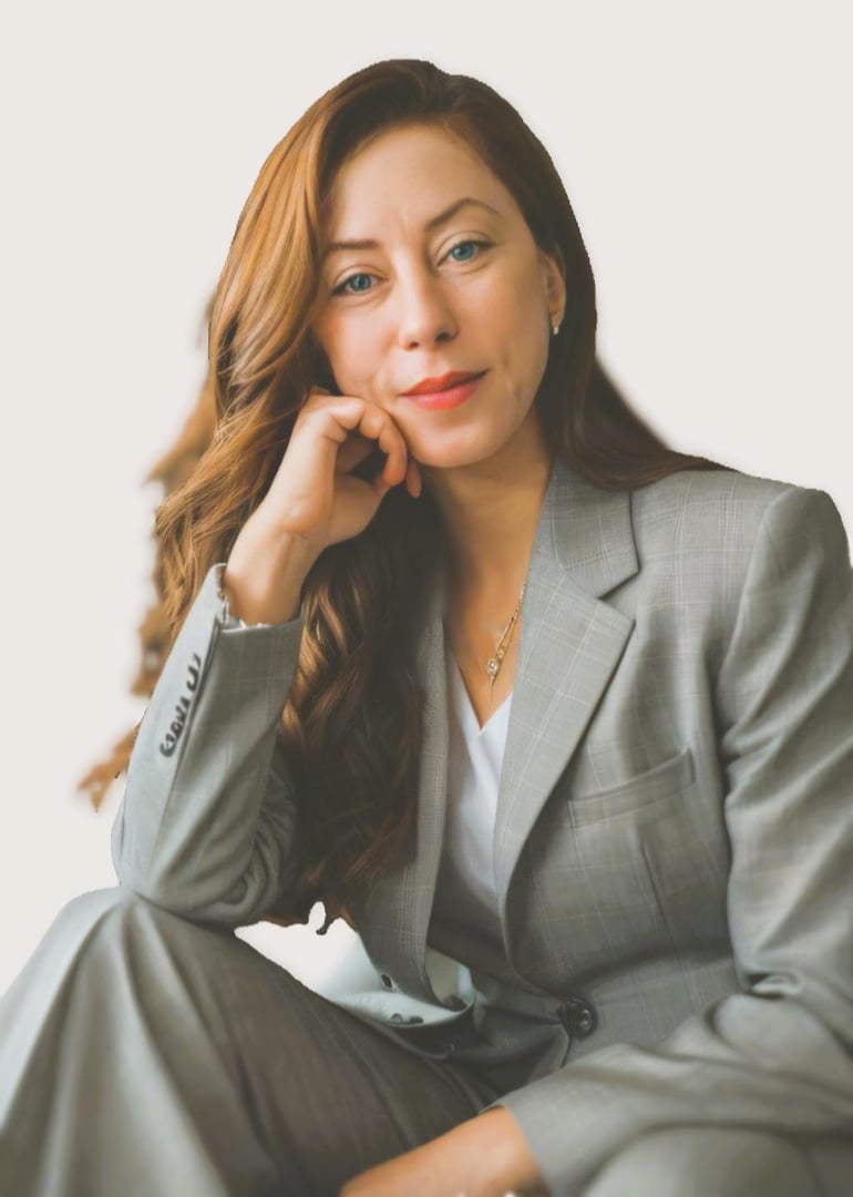 Woman with long hair in a gray suit seated, resting her chin on her hand, looking at the camera with a neutral expression.