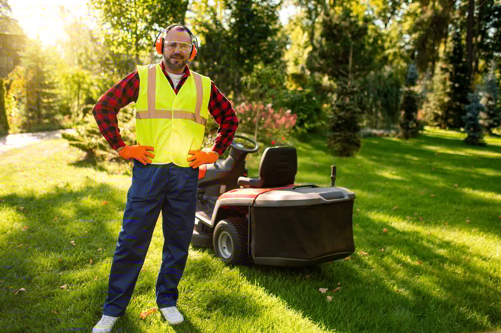 Lawn care worker standing with mower surrounded by fresh cut grass and plants