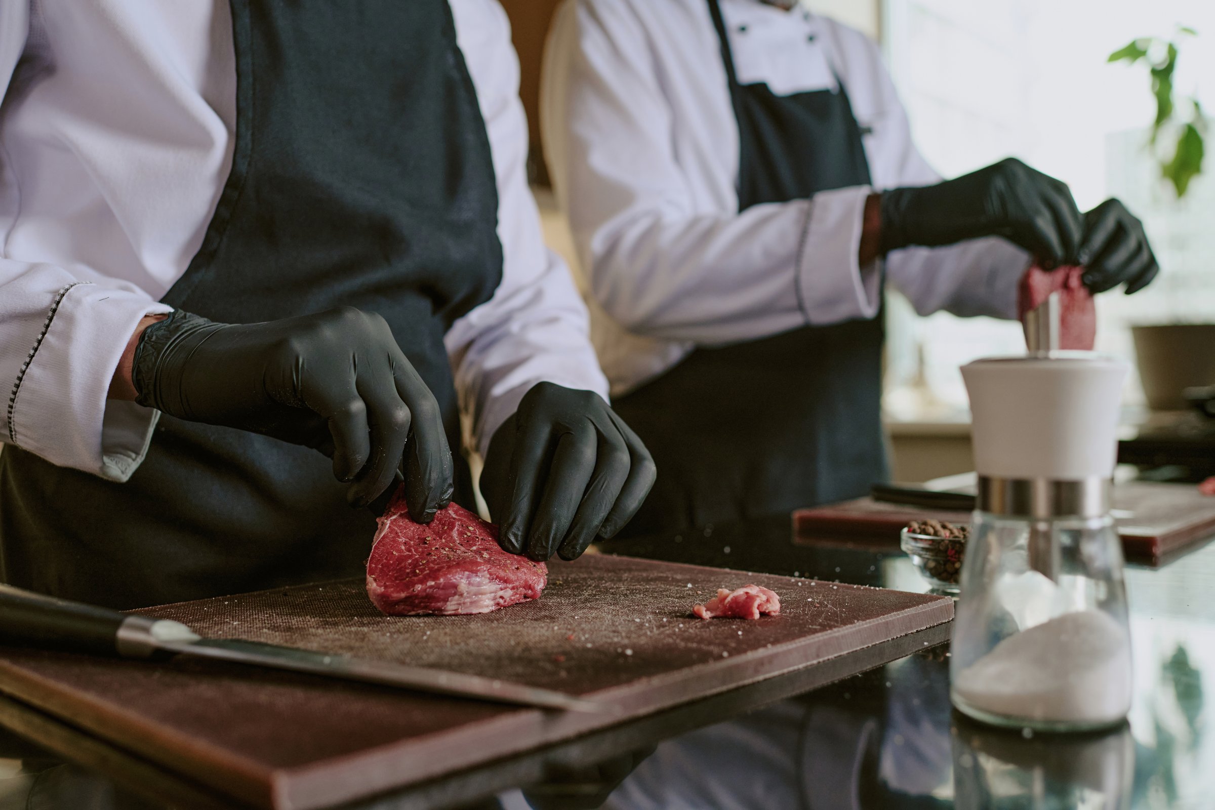 Medium close up of unrecognizable male hands in black latex gloves holding meat while adding condiment