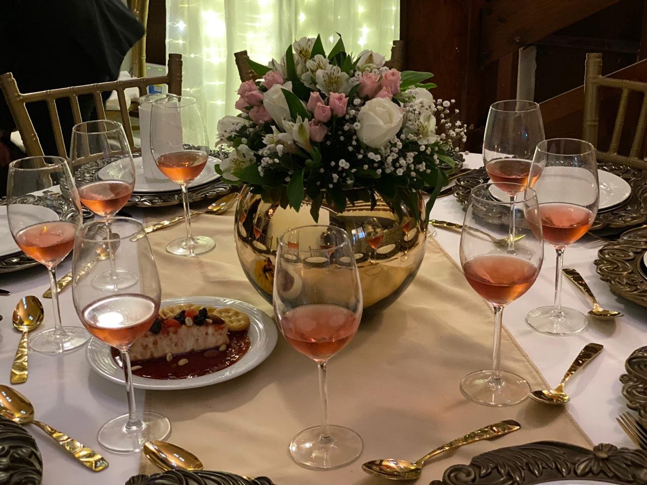 Elegant table setting with rosé wine glasses, dessert plates, and a floral centerpiece in a gold vase.