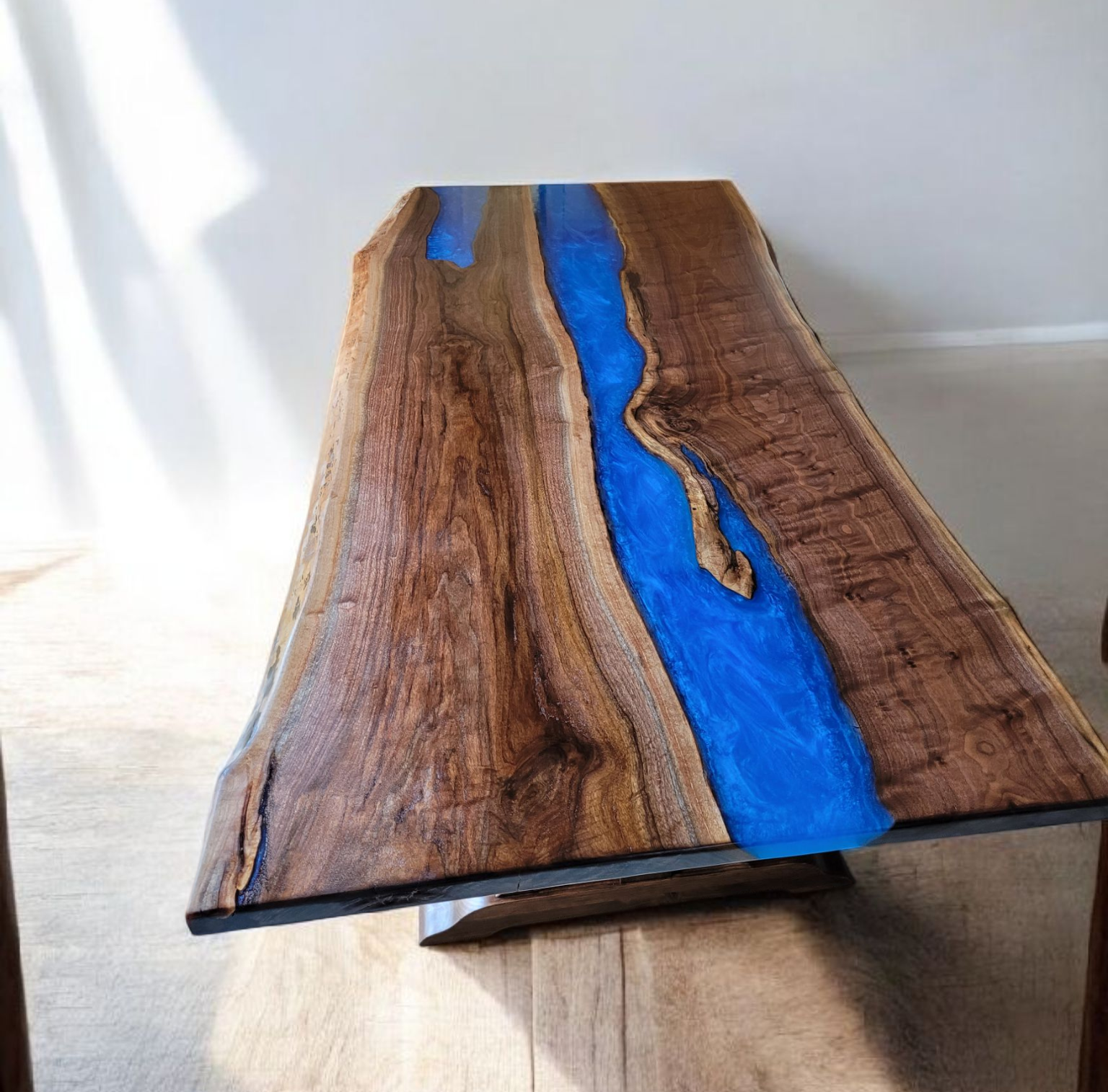 Live edge wood table with a blue resin river design running through the center, set on a light wood floor.