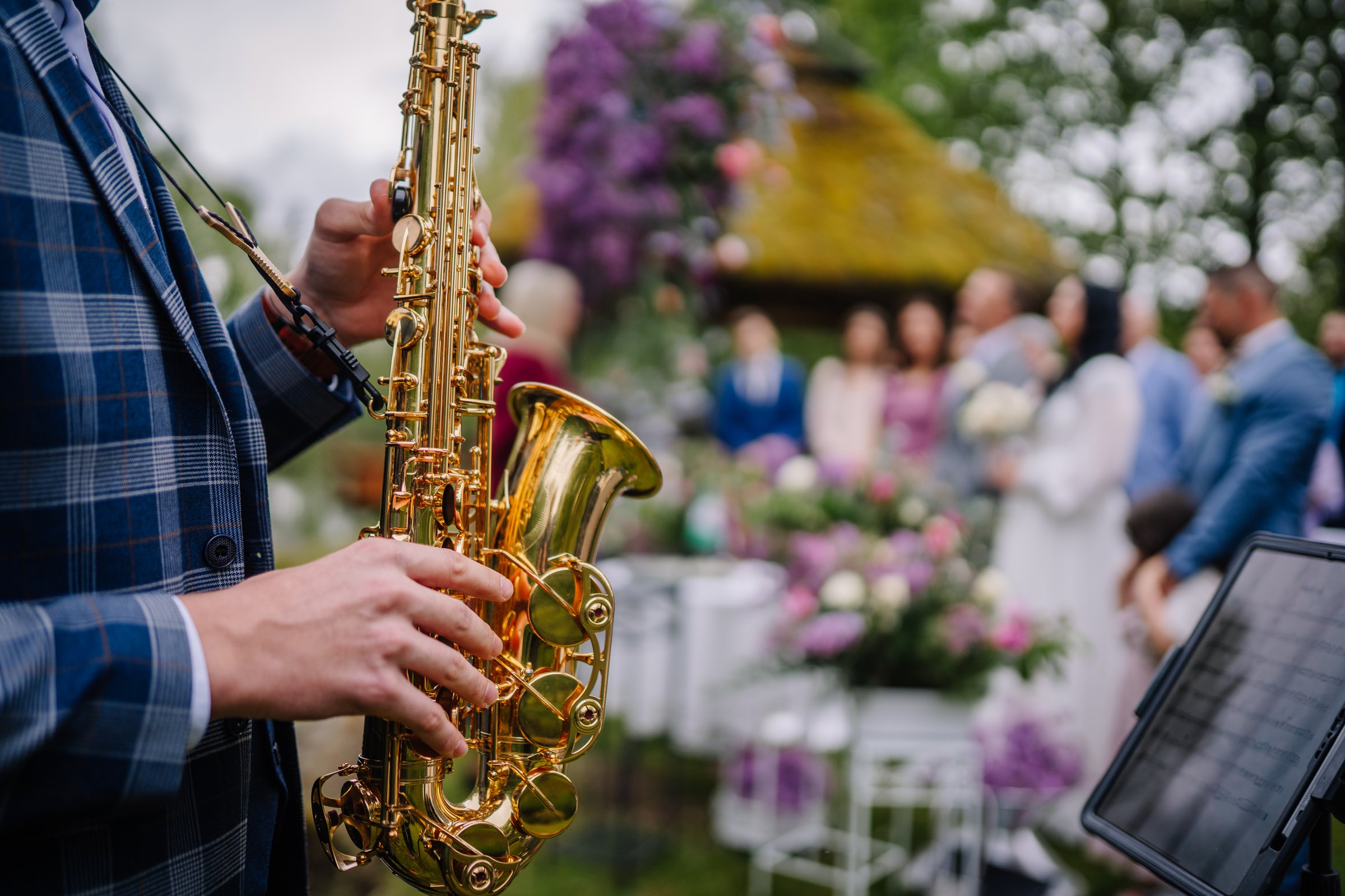 Valmiera, Latvai - May 23, 2025 - Close-up of a saxophonist playing at an outdoor wedding ceremony, with blurred guests, flowers, and decorations in the background.