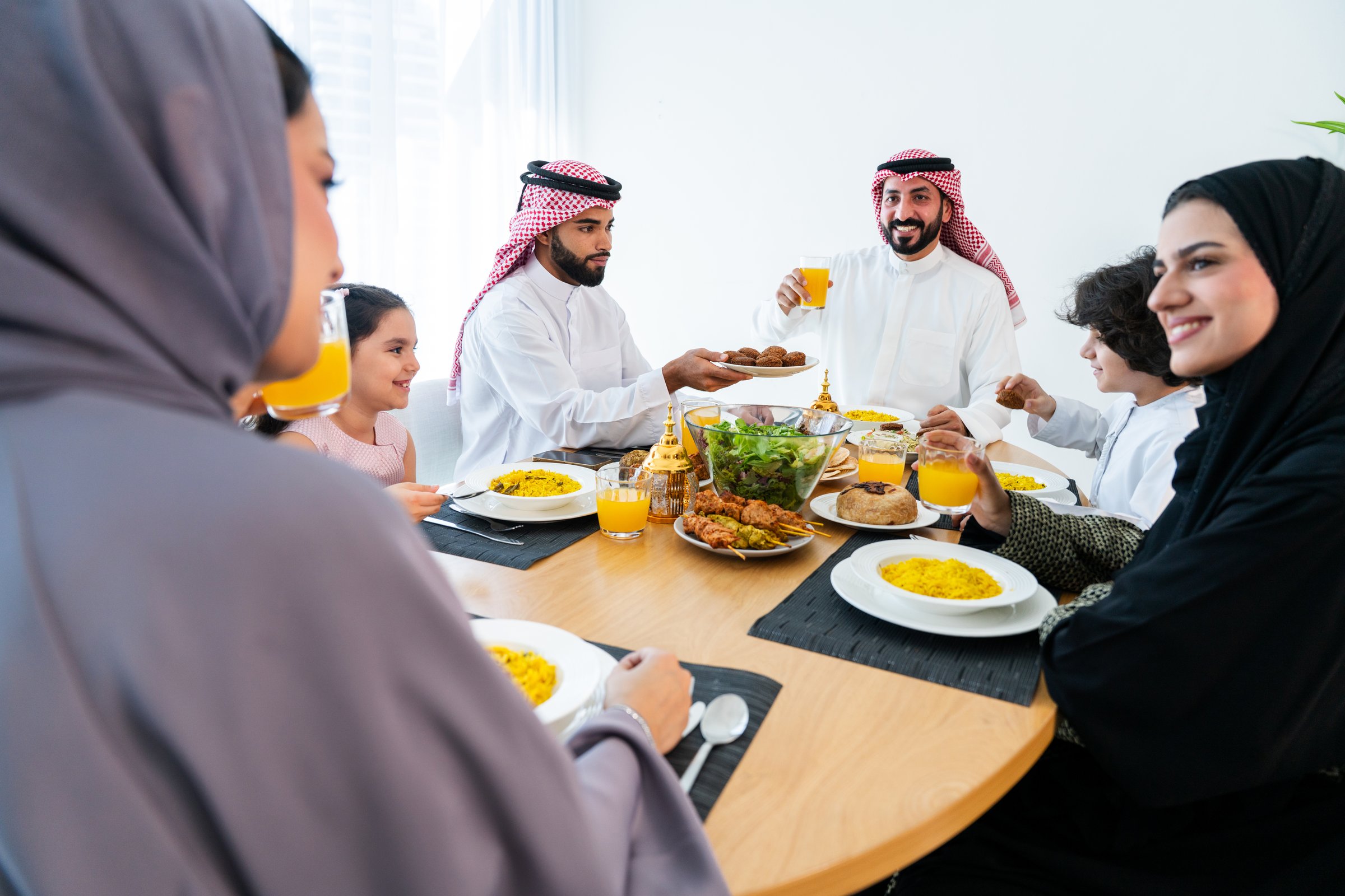 Happy arab family wearing saudi arabia clothing spending time together at home during dinner - Middle-eastern saudi parents and children celebrating ramadan after day fasting
