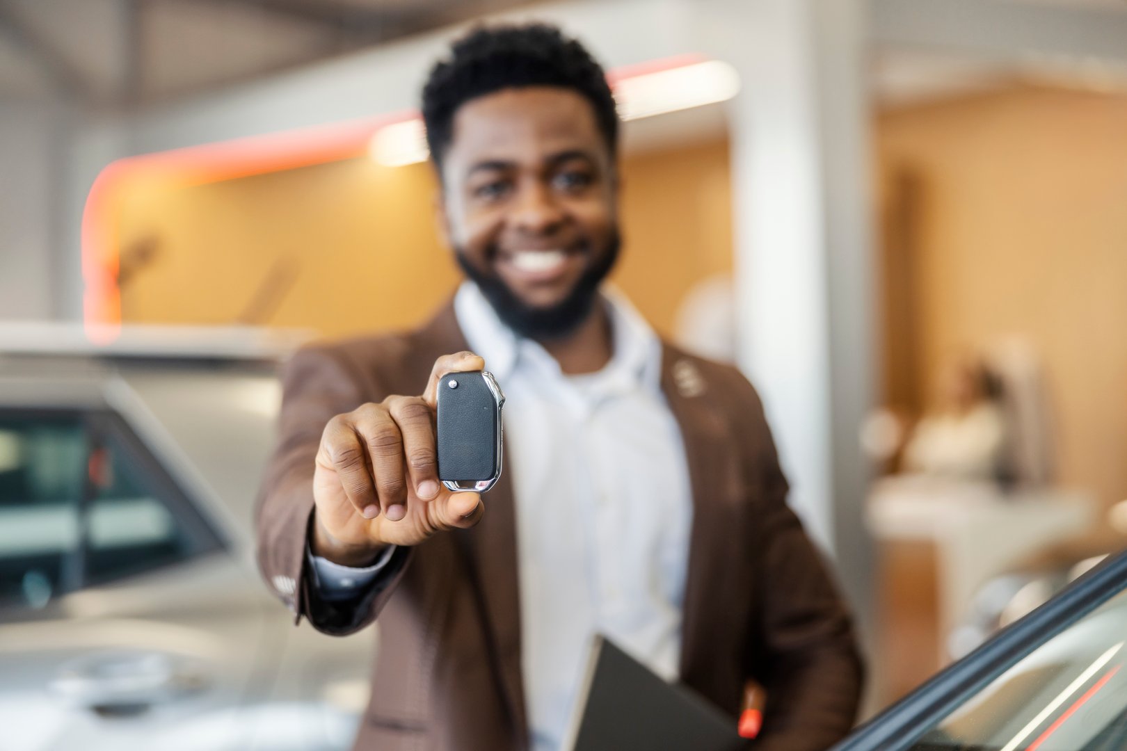 Selective focus on interracial car dealer's hand showing car keys at camera at car salon.