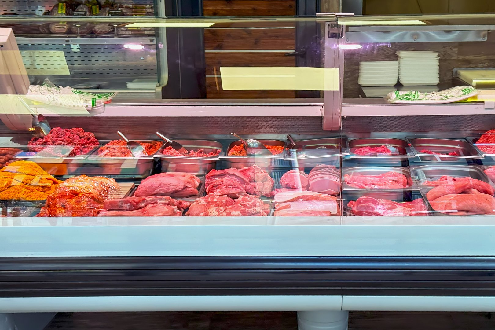 Variety of fresh raw meats and minced products displayed in a butcher shop counter. Concept of meat freshness, food quality, traditional butcher meat selection