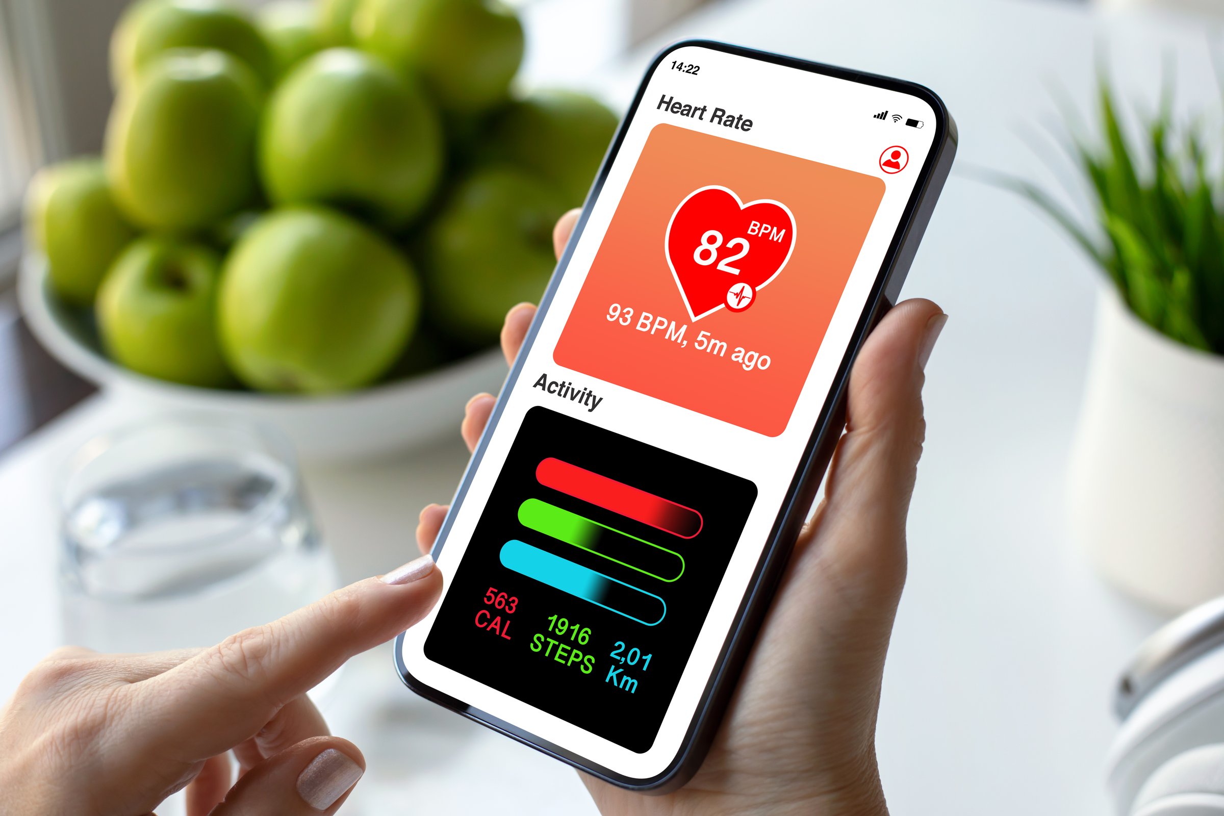 woman hand hold phone with app heart and activity on screen background of green apples in cafe