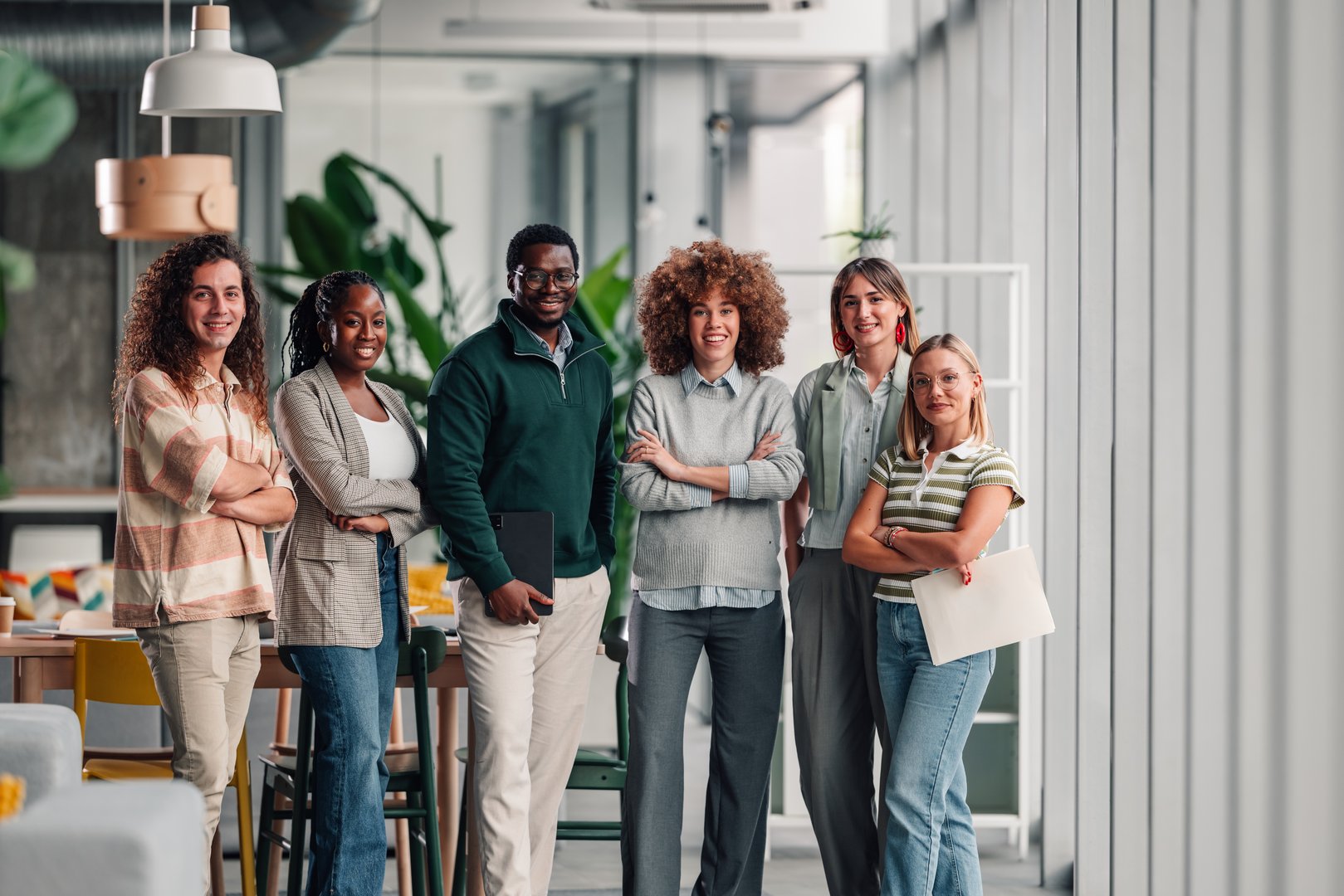 Group of diverse business professionals standing with arms crossed, smiling at camera in a bright, modern office space