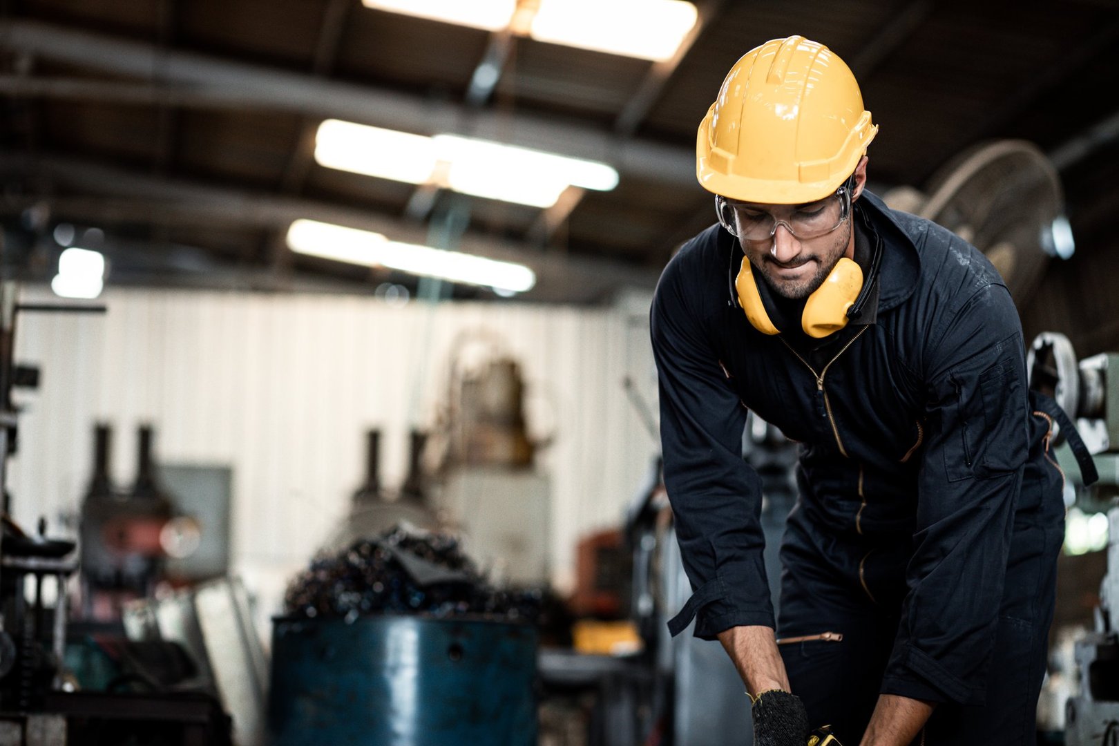 Closeup side view worker wearing uniform and protective helmets using machine is working hard in the factory. Staff operate control heavy machine in factory