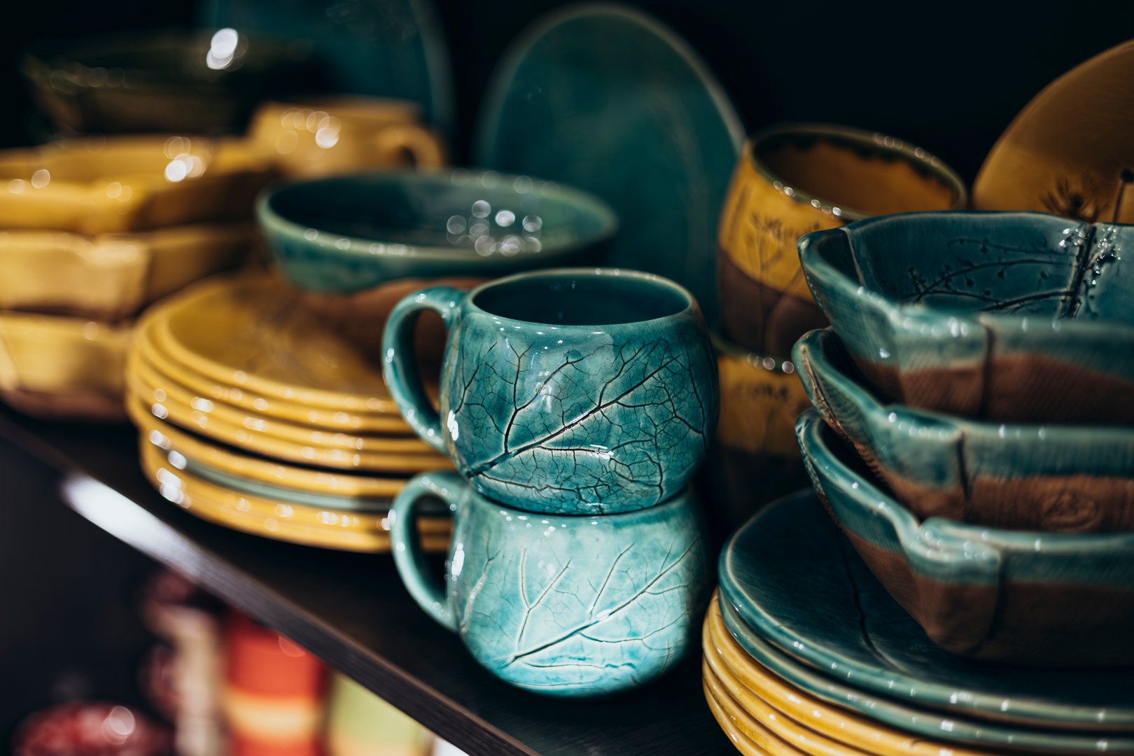 Ceramic cups and plates with imprints of real leaves. Colorful handmade dishes, plates, ceramics. Souvenir shop with ceramic plates. Dishes with floral ornaments.