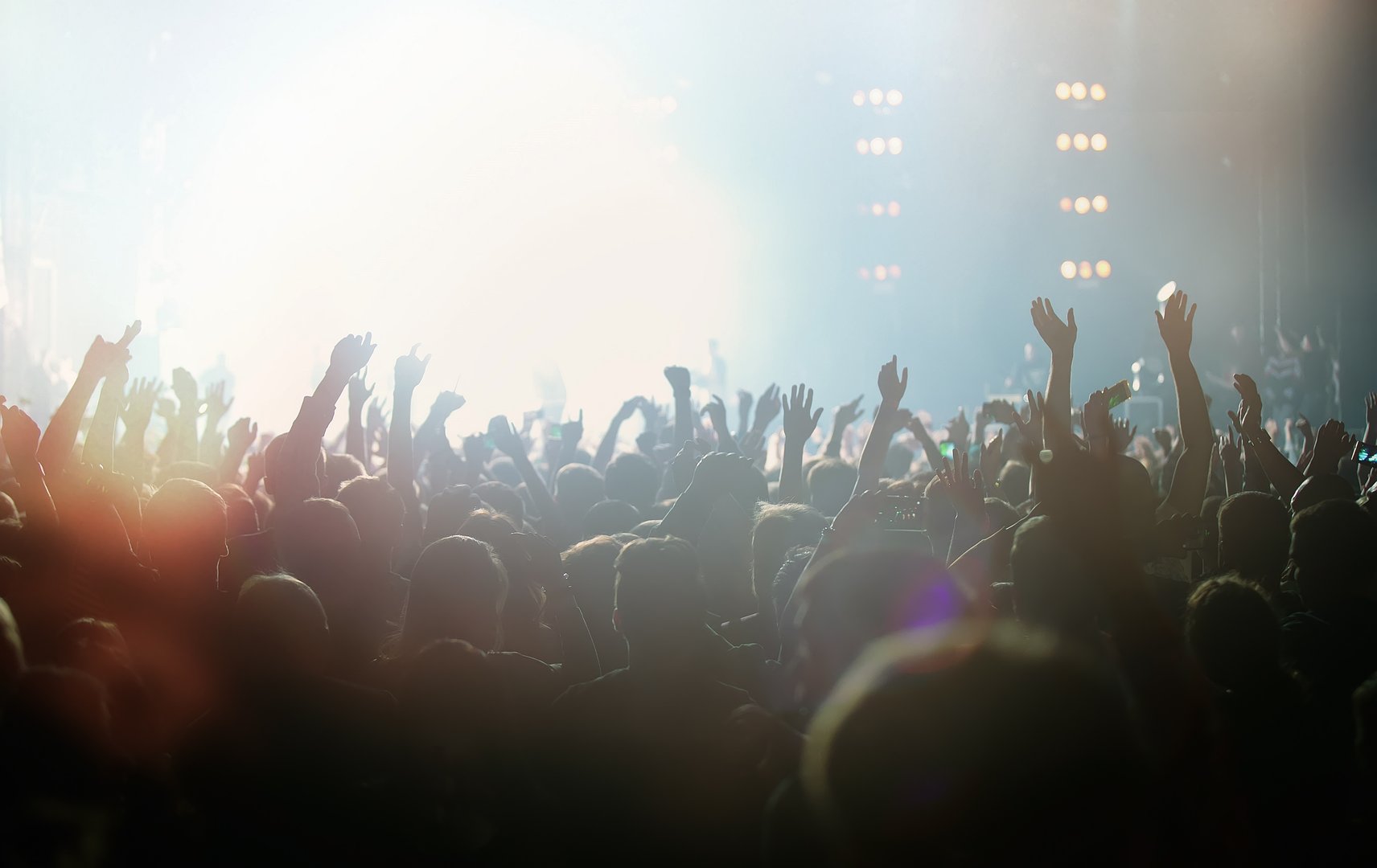 Sea of hands on popular music concert in big music hall. Crowd of cheerful young people partying on dance floor