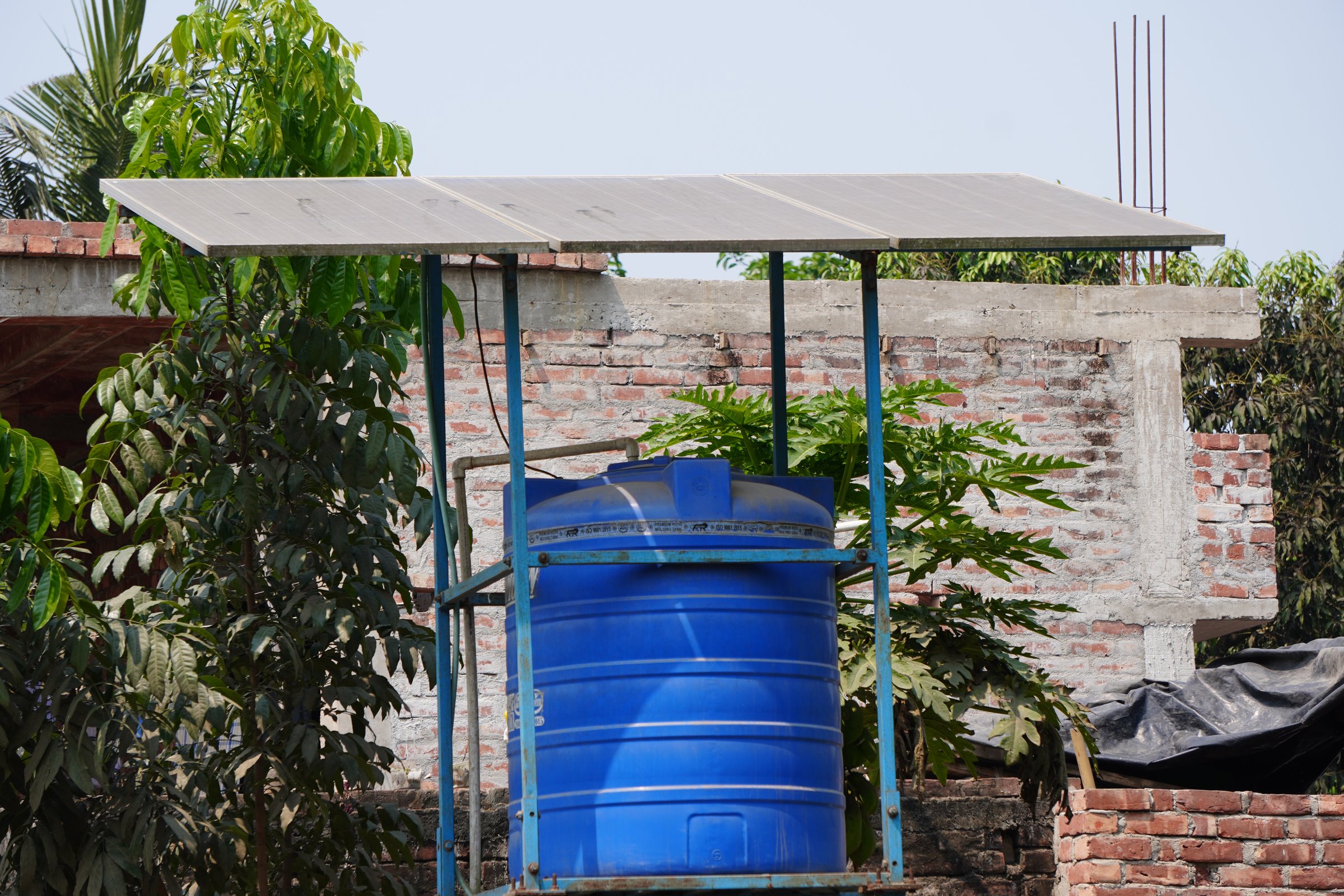 A blue water tank with a solar panel roof structure beside a newly constructed building