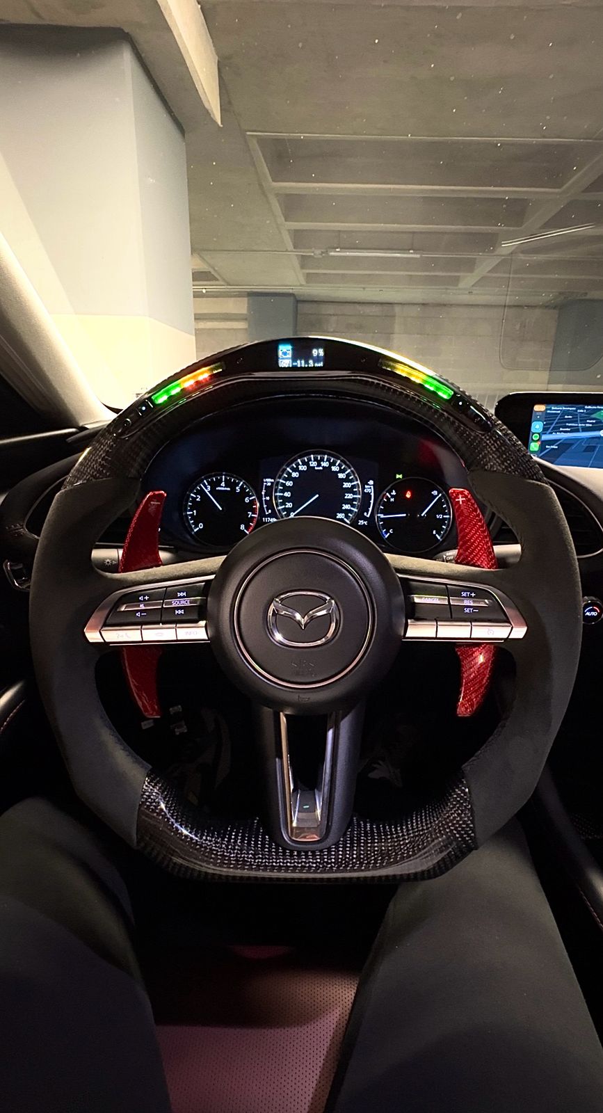 View of a Mazda steering wheel with red paddle shifters, dashboard, and illuminated indicator lights in a parked car.