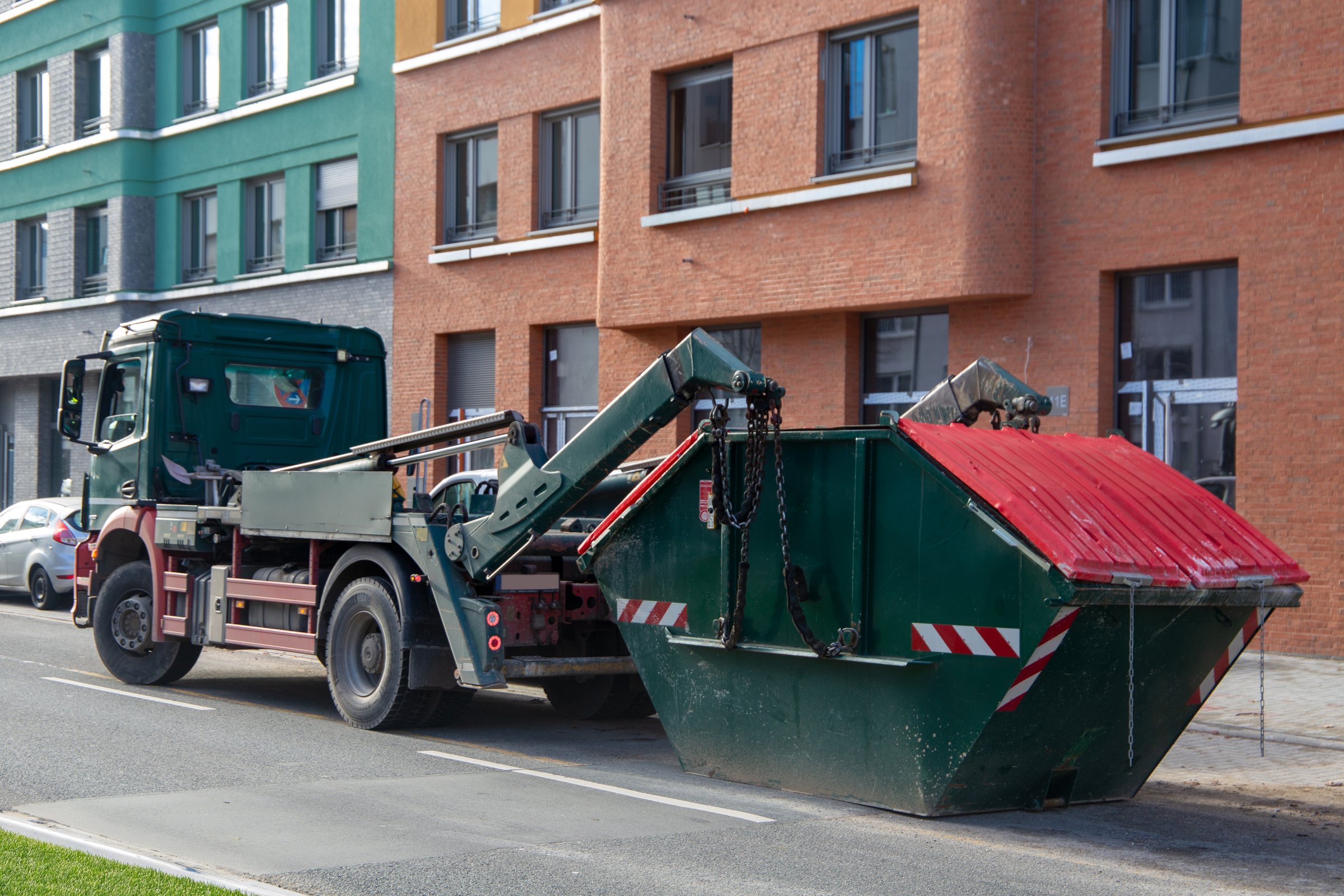 Container service: Lorry with skip container in front of a new apartment building