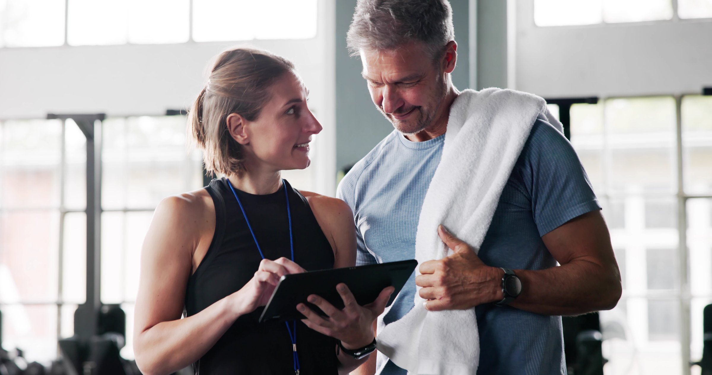 Fitness Trainer Instructor Showing Notes On Clipboard To Woman In Gym