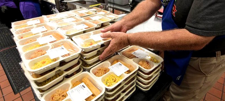 Person organizing stacked trays of packaged meals in a kitchen setting.