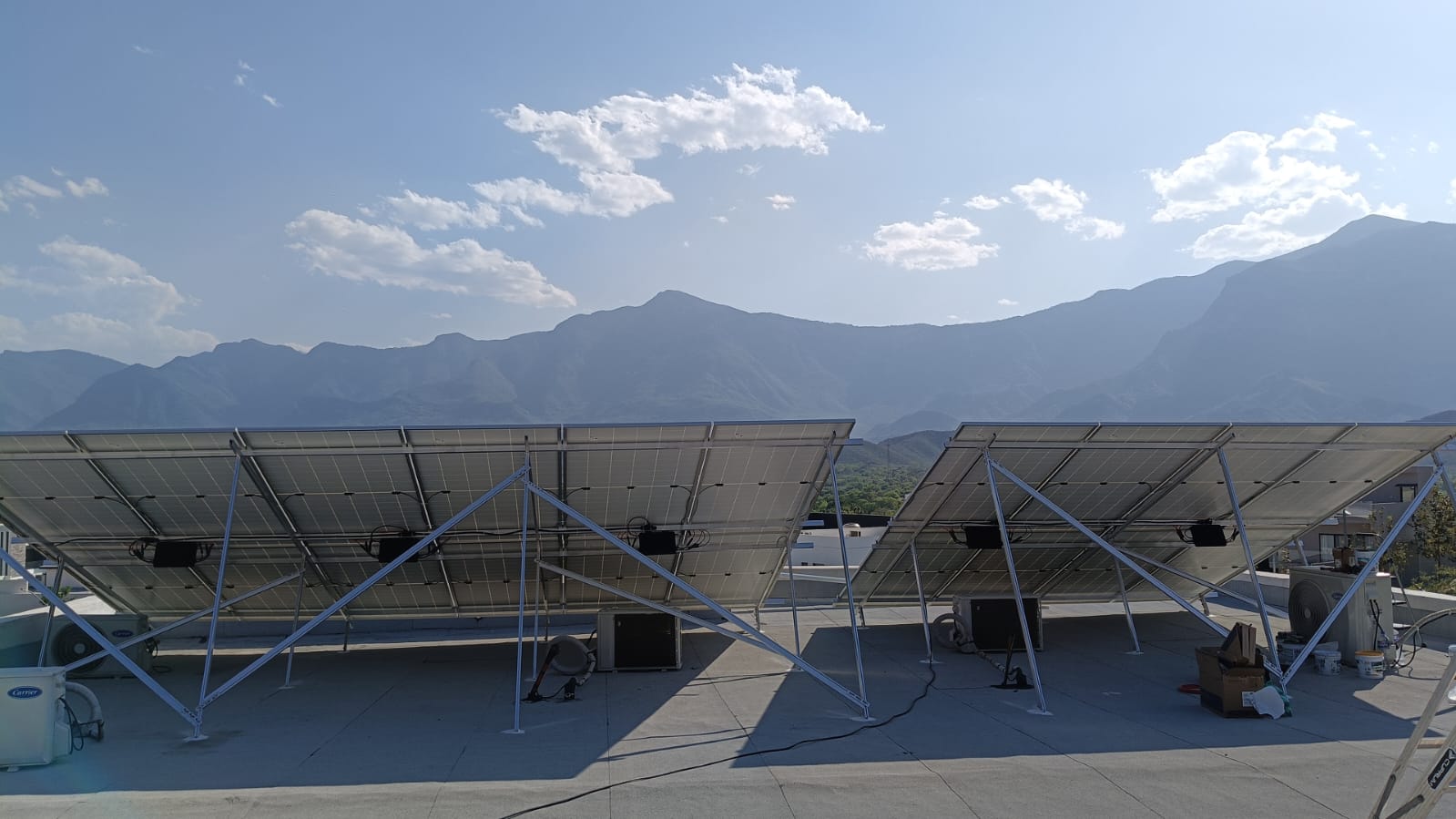 Two solar panels on a rooftop with mountains and a clear sky in the background.