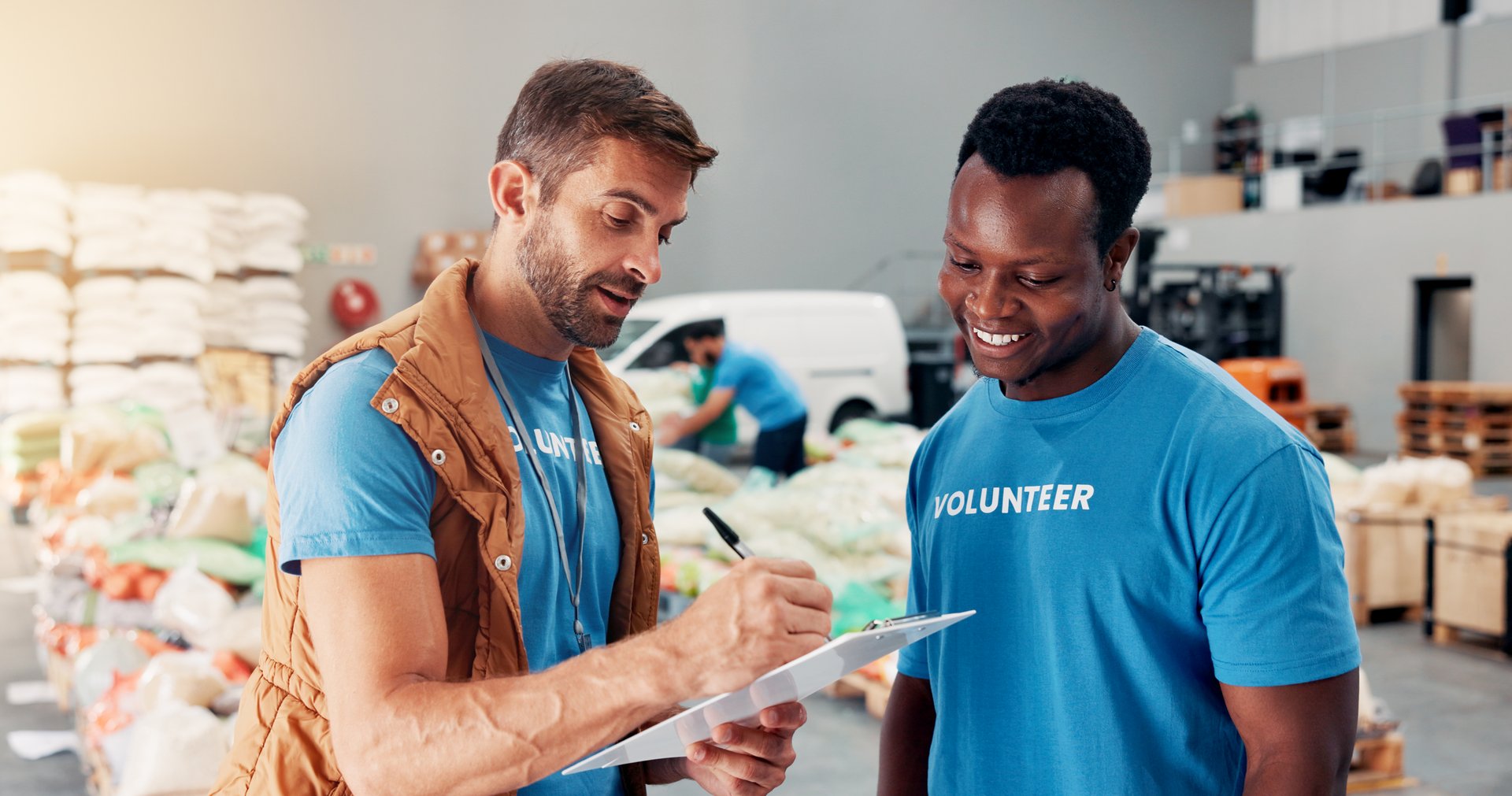 Men, volunteer and writing on clipboard at warehouse of donation stock, inventory checklist and charity. People, team and grocery notes for humanitarian aid, ngo welfare and food list of distribution