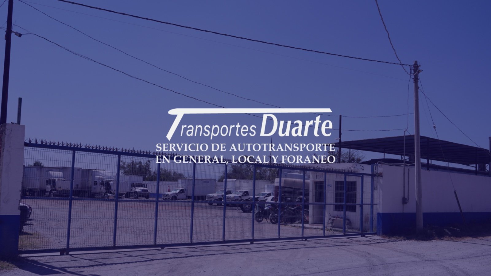 Transportes Duarte facility entrance with gate and parked trucks in the background.
