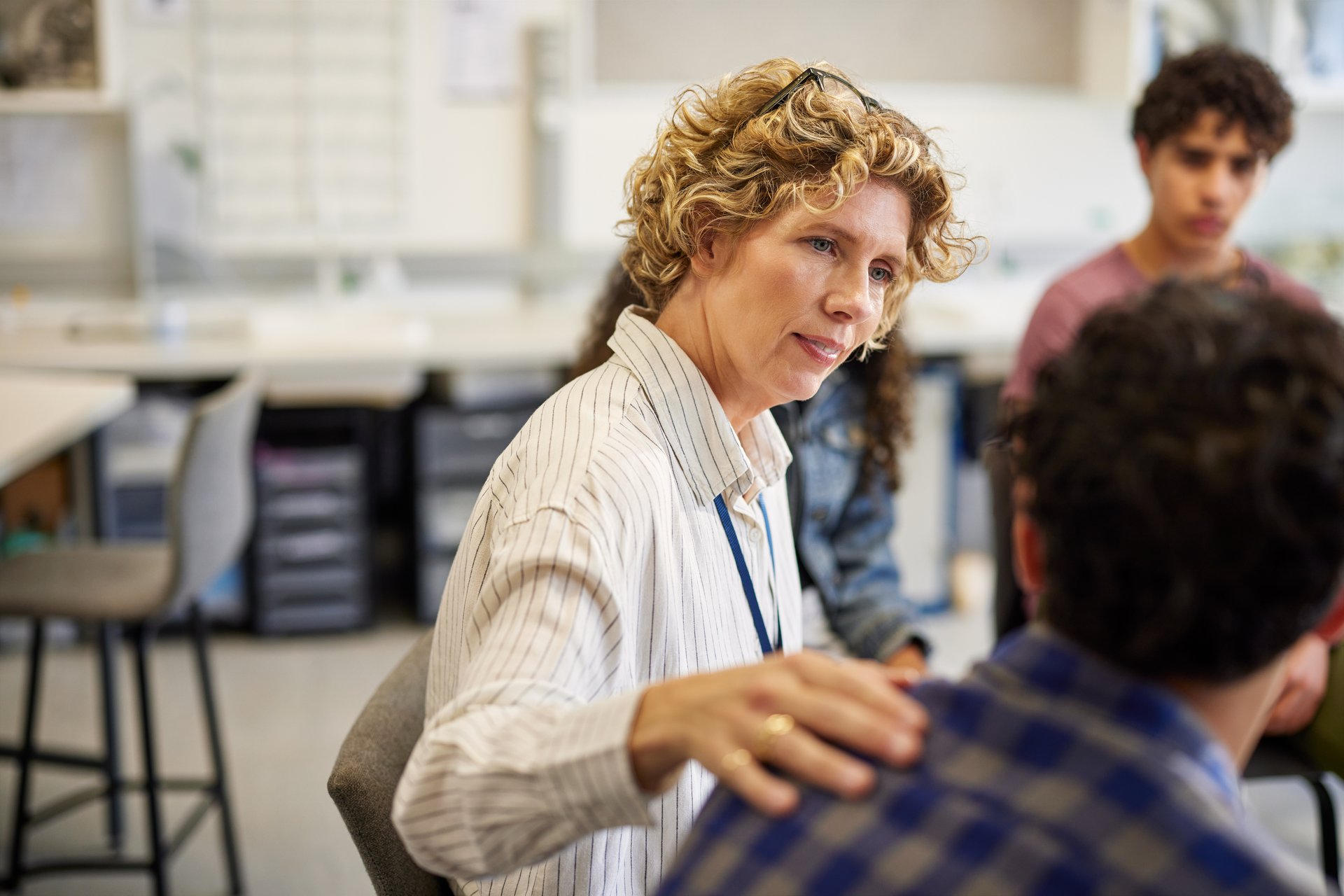 Female mature educator offering a comforting gesture to a male student during a counseling session at high school. Empathetic interaction focused on emotional support and mental well-being at secondary school. Distressed teenager boy crying and sharing mental health troubles during support group session.